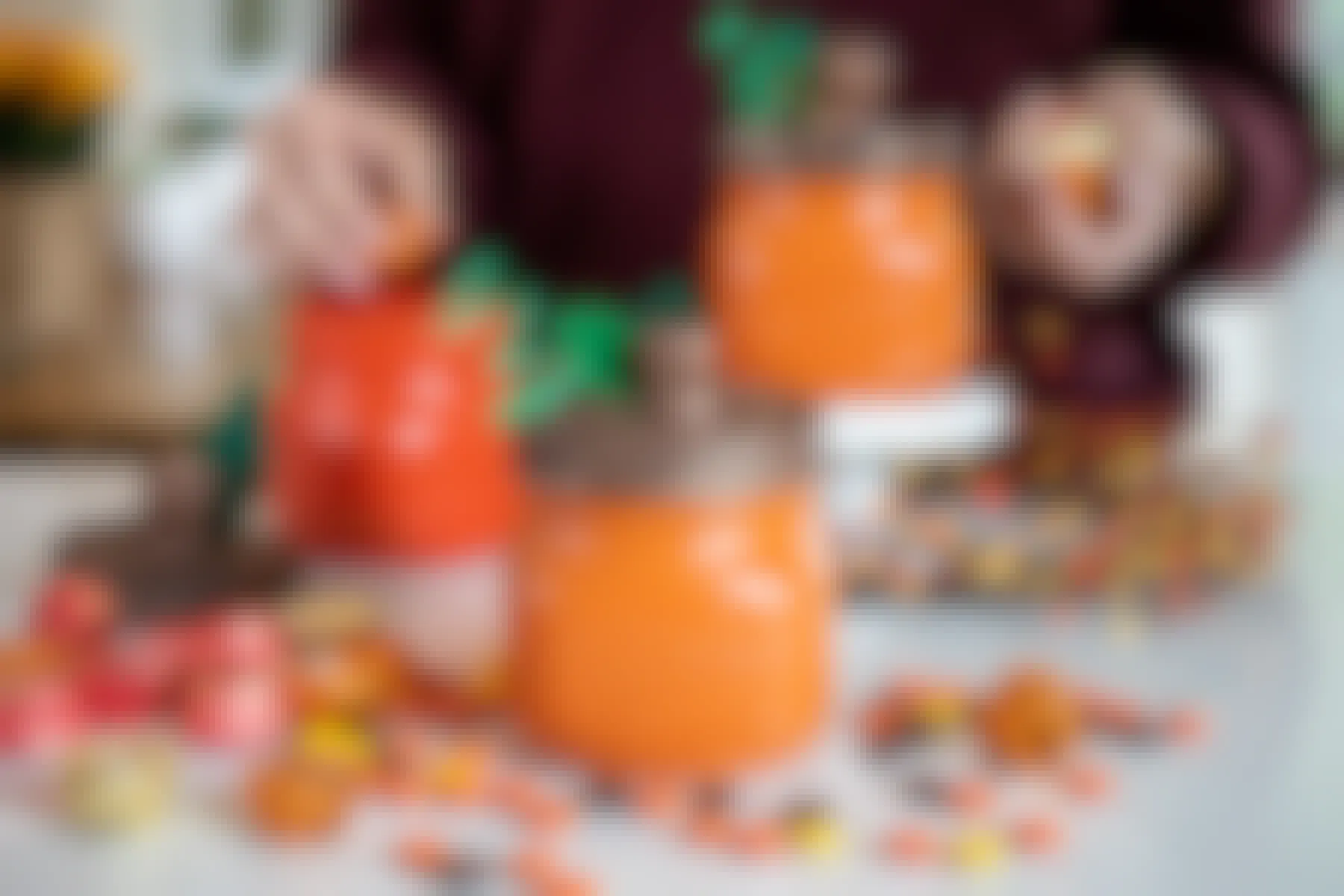 A person putting candy into mason jars that have been decorated to look like pumpkins.