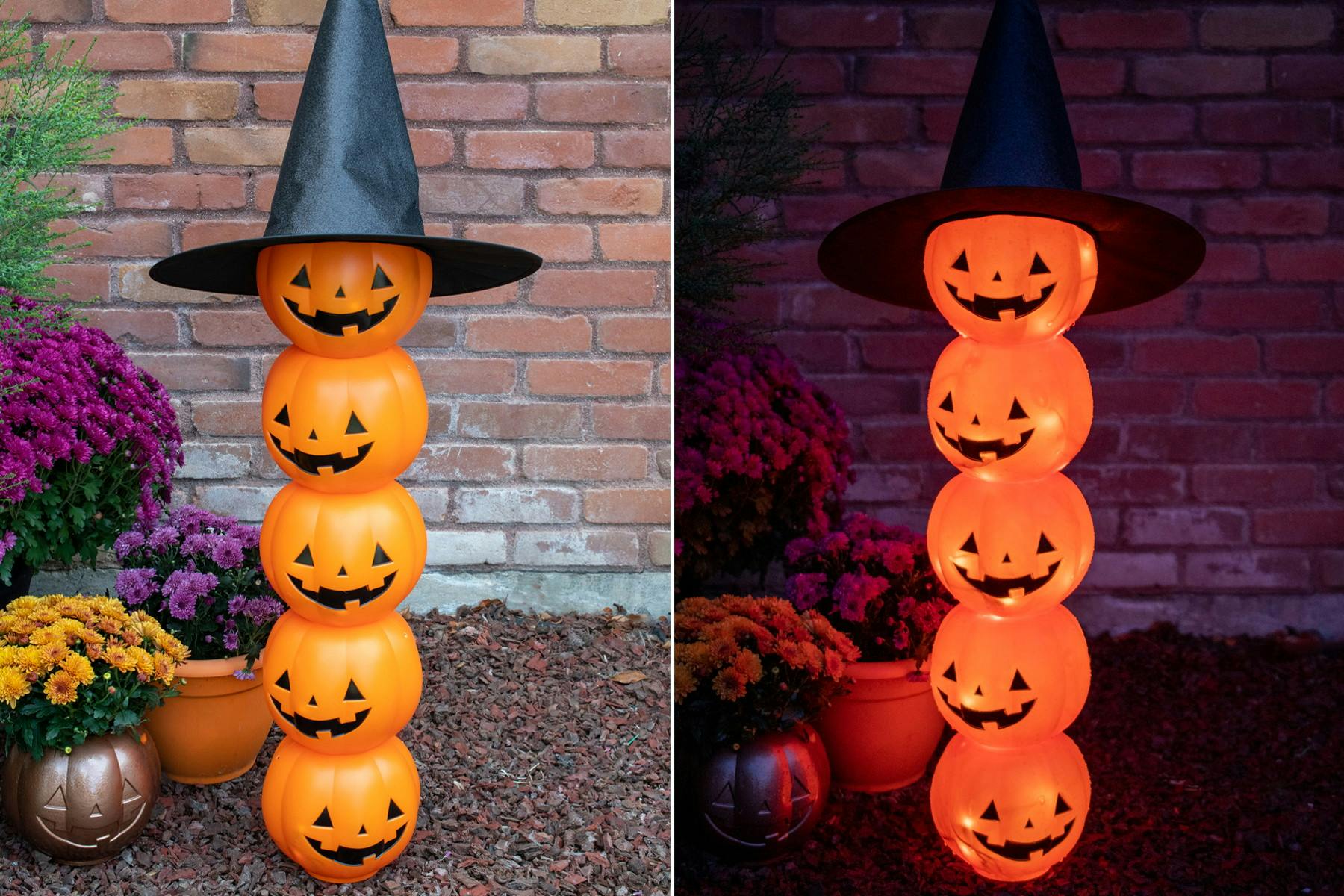 A light-up Halloween pumpkin totem made from plastic trick-or-treat pumpkin pails and a witch hat set up in a garden.