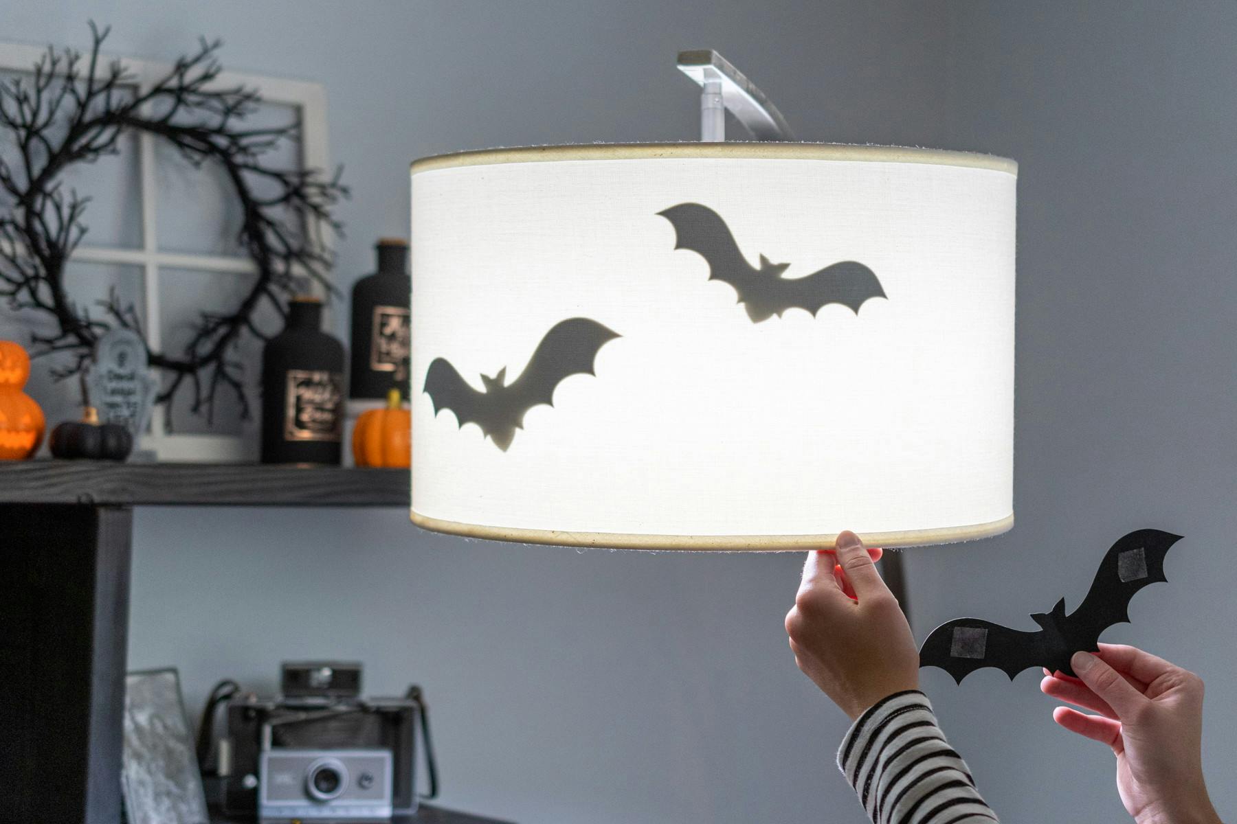 A person attaching bat cutouts to the inside of a lamp shade with double sided tape.