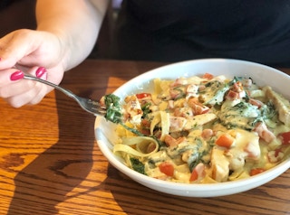 a fork with food on it scooped out of a bowl of pasta 