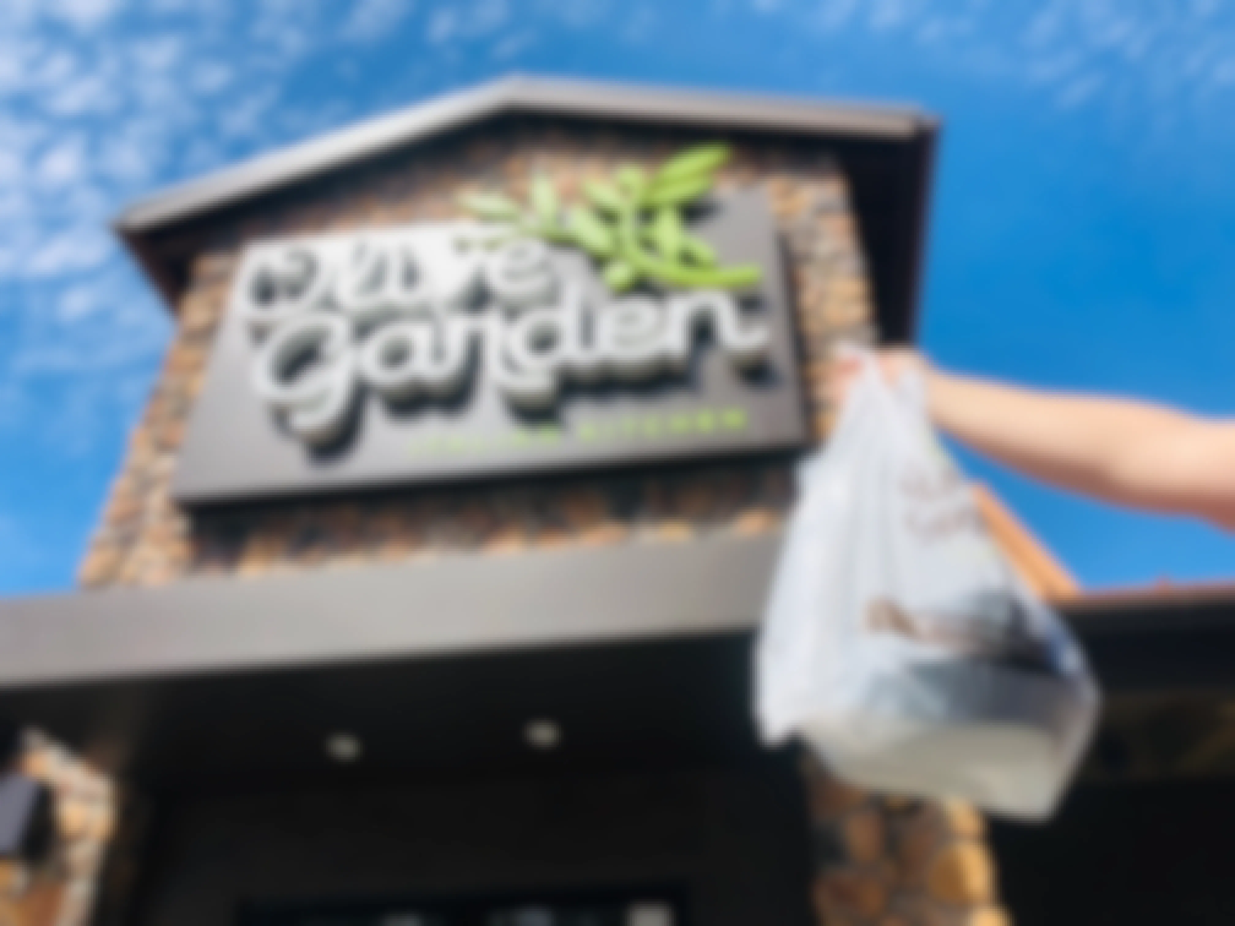 woman holding a bag of olive garden takeout in front of Olive Garden restaurant