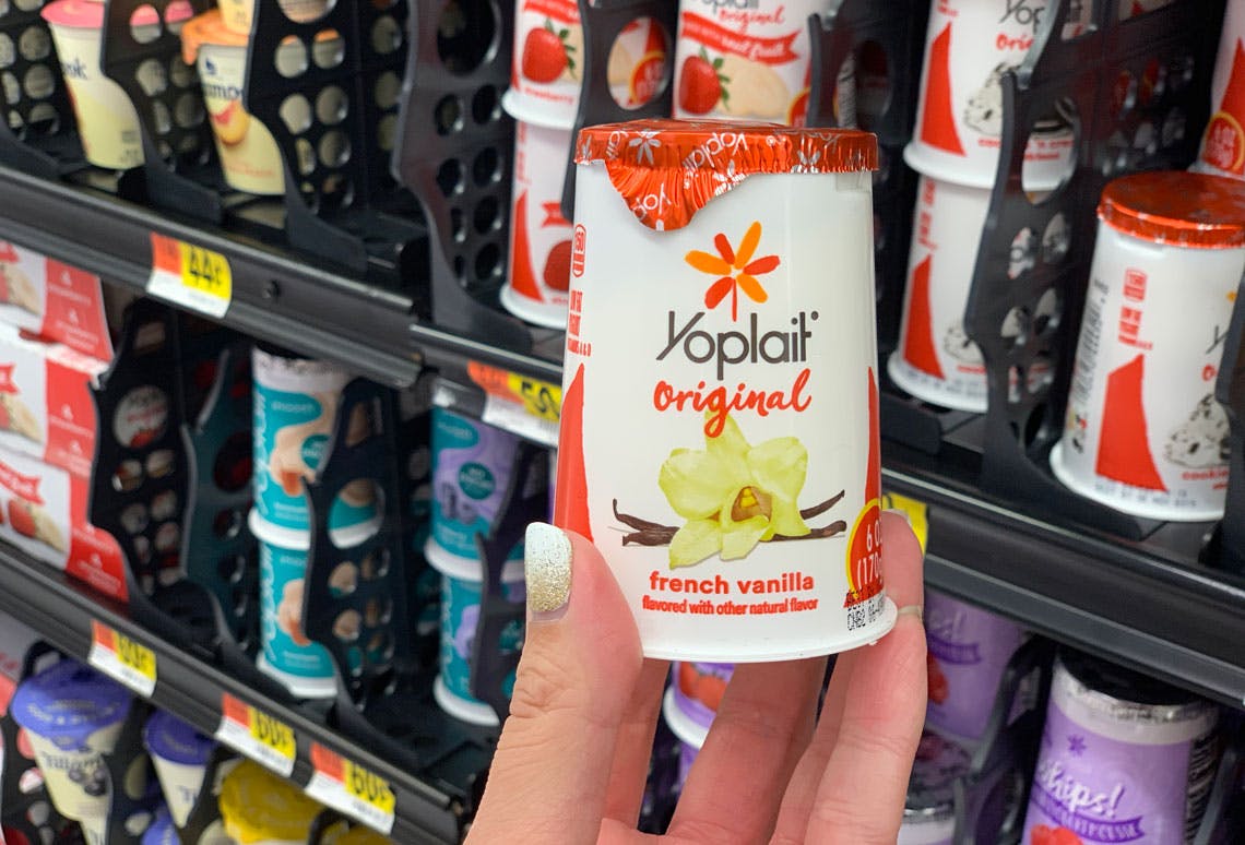 A container of Yoplait original french vanilla yogurt being held up in front of a shelf of more yogurt at Walmart.