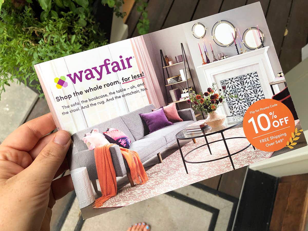 a person's hand holding a wayfair coupon for 10% off