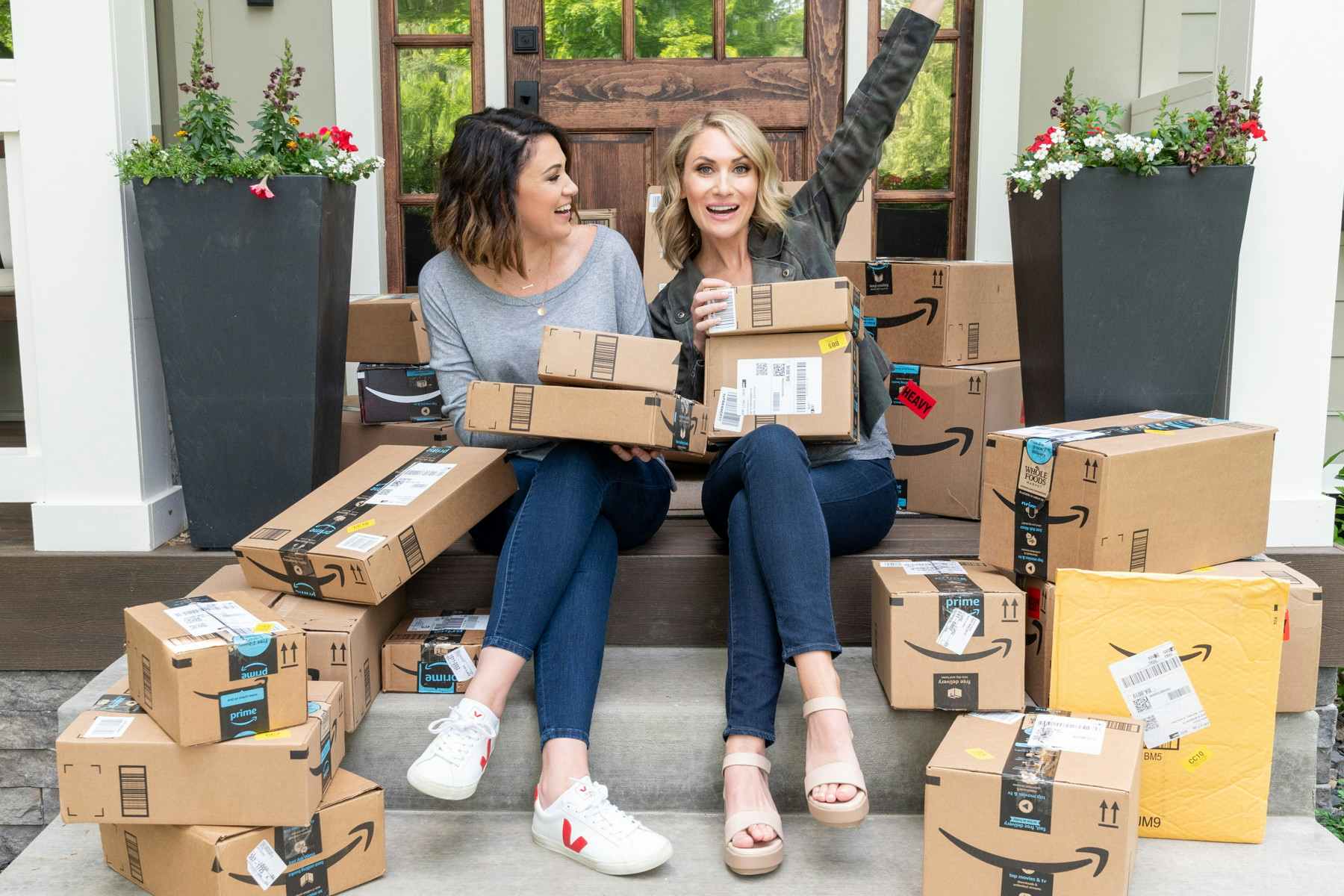 Two women sitting on porch steps filled with amazon boxes.