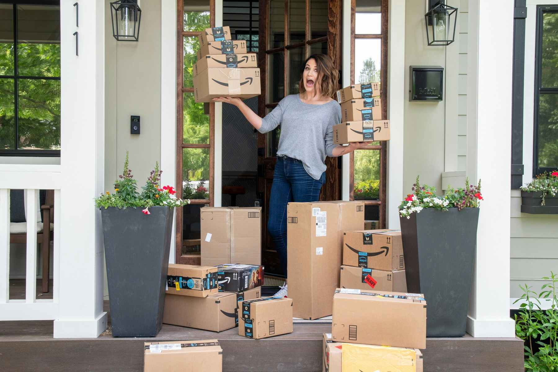 A woman excitedly holding amazon boxes on a porch full of boxes