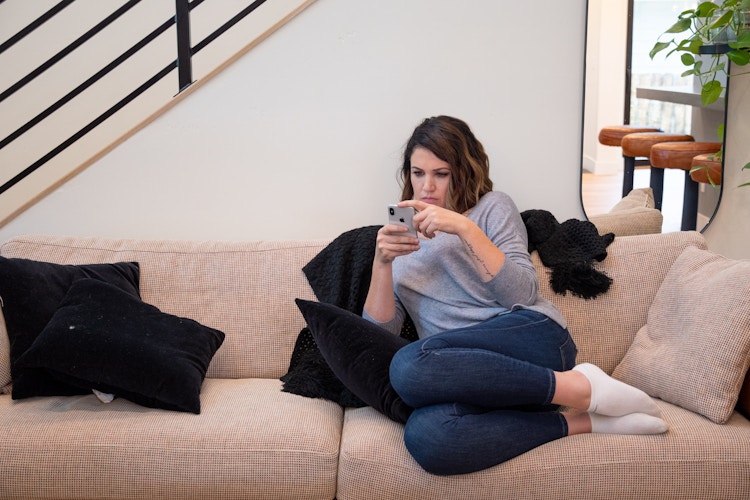 A woman looking at a cell phone while sitting on a sofa.