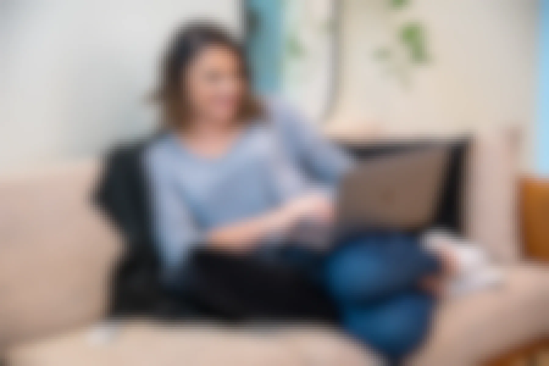 A woman sitting on a sofa looking at a laptop computer