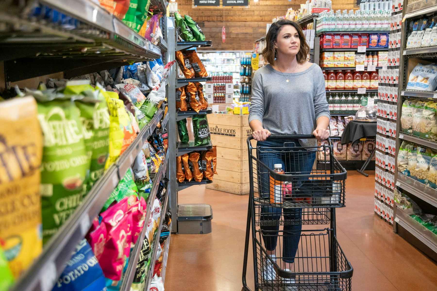 A woman pushing a shopping cart down an aisle at Whole Foods.