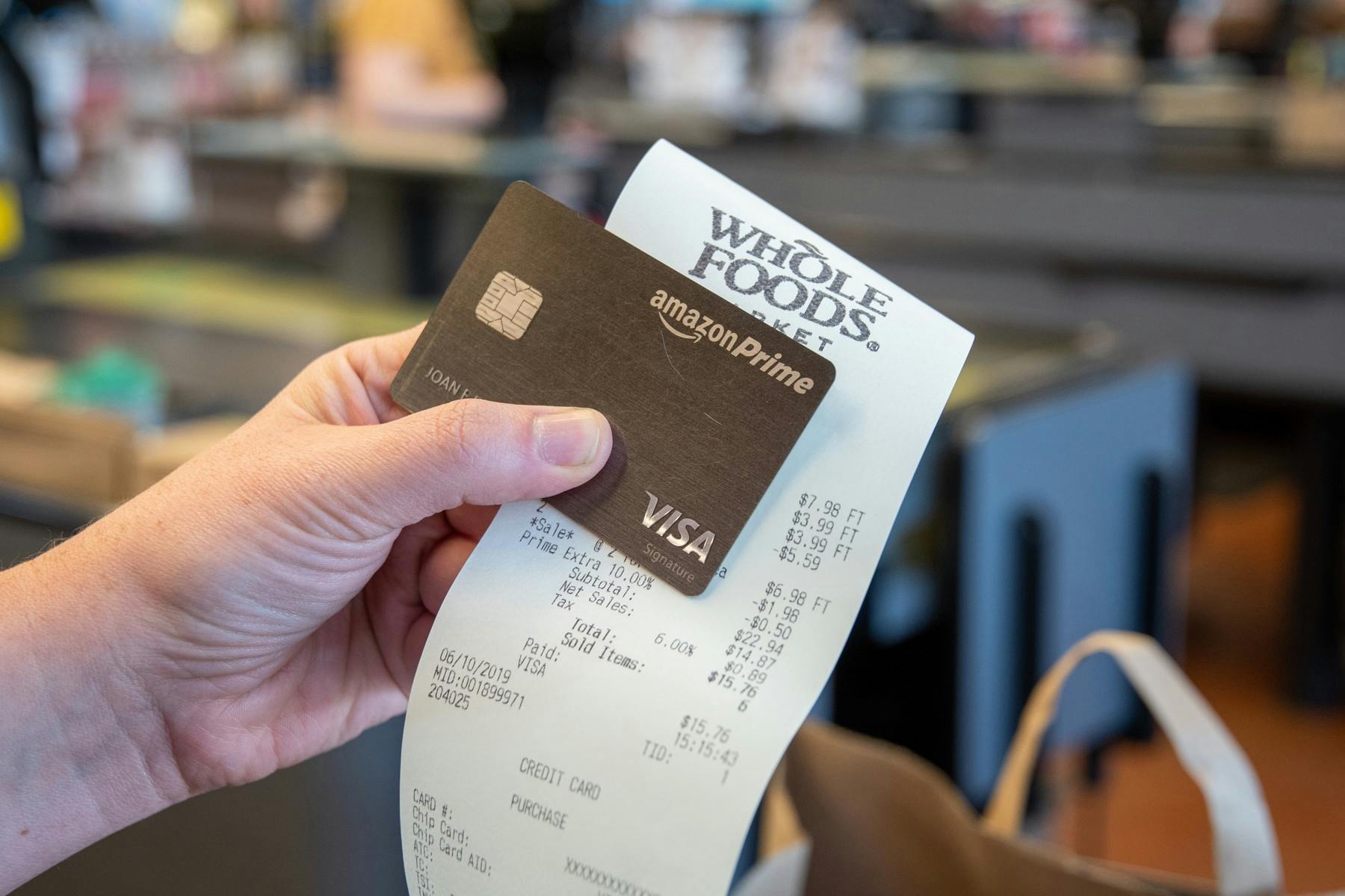 A hand holding an Amazon Prime Visa credit card and a Whole Foods receipt.