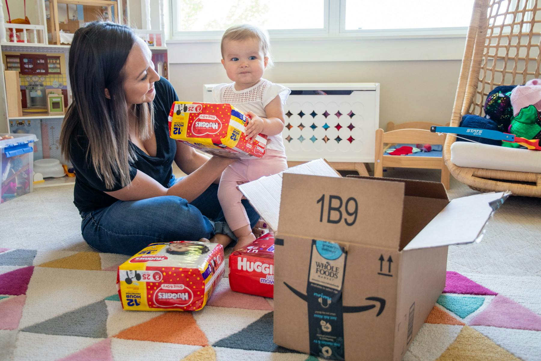 A mom sitting on the floor with her baby, surrounded by packages of Huggies diapers and an Amazon box.