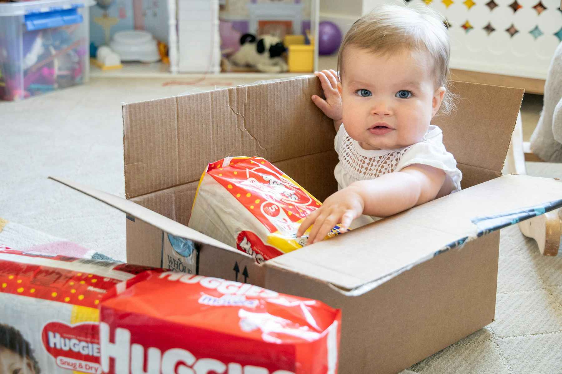 cute baby sits inside a box with huggies around her