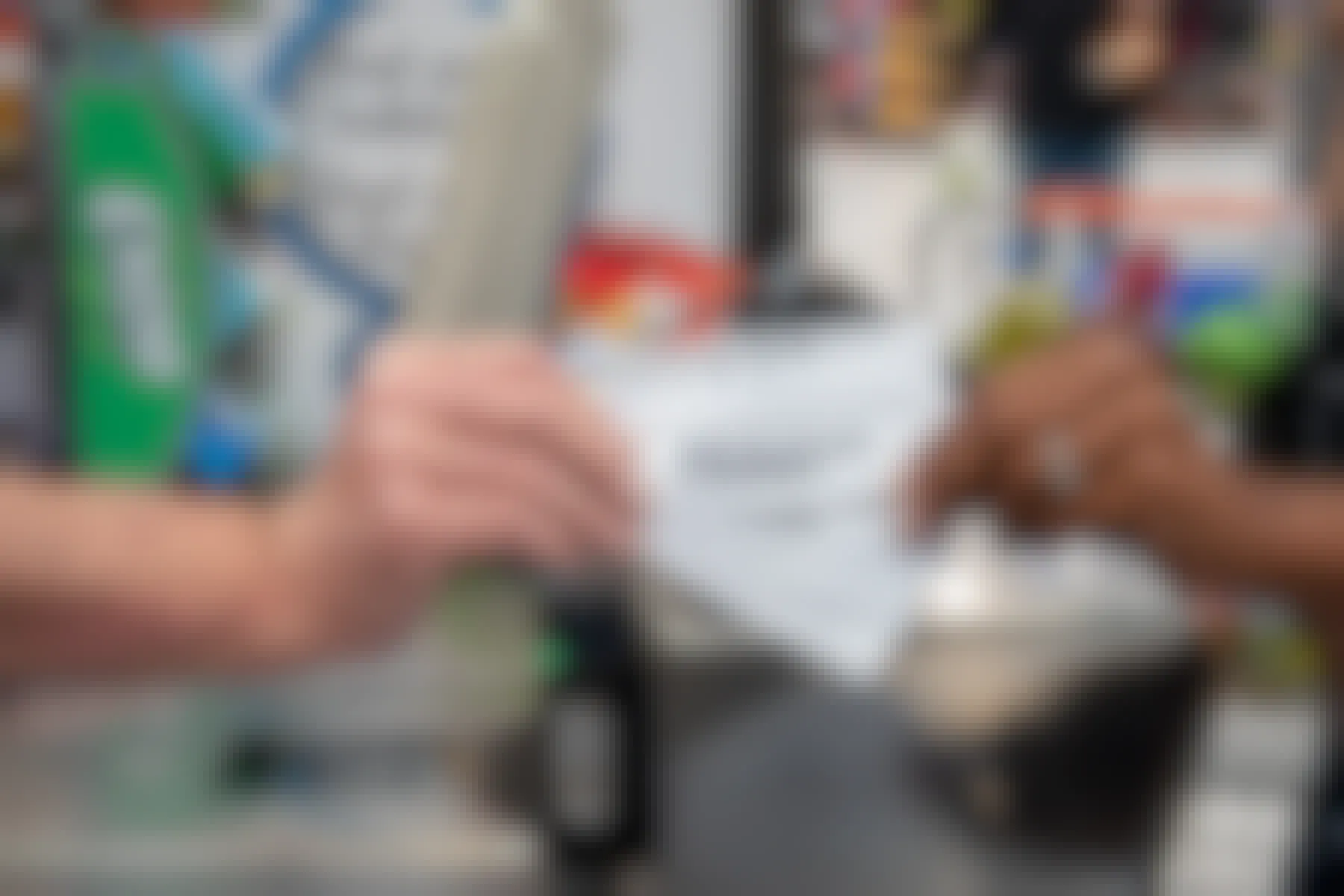 A person's hand giving a stack of printable coupons to the hand of a grocery store cashier in front of the checkout scanner.