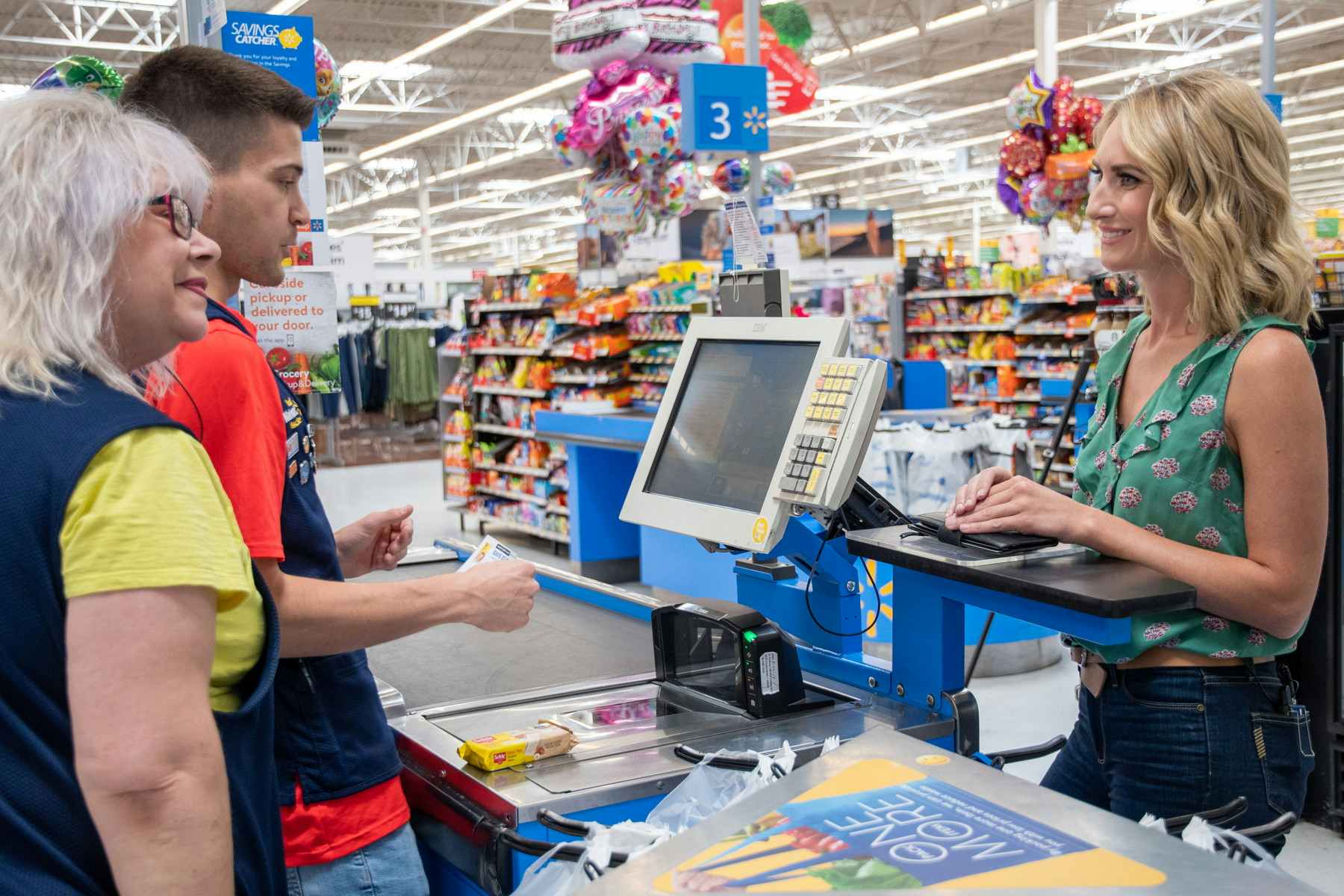 A woman standing at the checkout lane at Walmart and smiling at the cashiers who are helping her.
