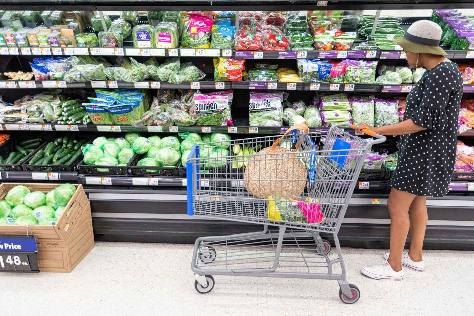 A person pushing a Walmart shopping cart and looking at the produce on the shelves.