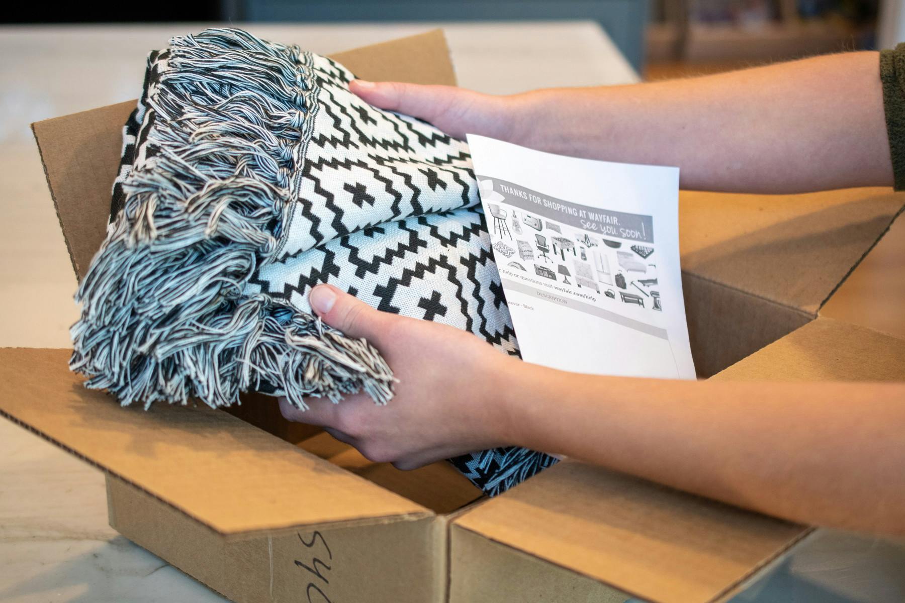 a woman taking a wayfair rug out of its package with a return slip right on top of it