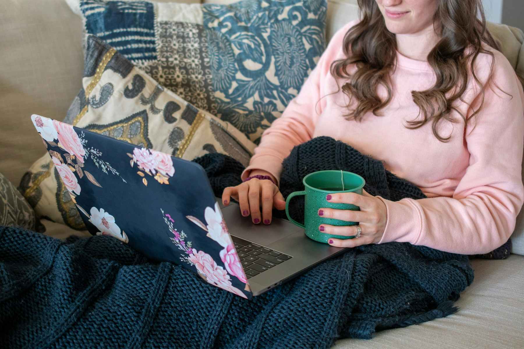 Woman sitting on a couch, looking at a computer with a cup of tea in hand.