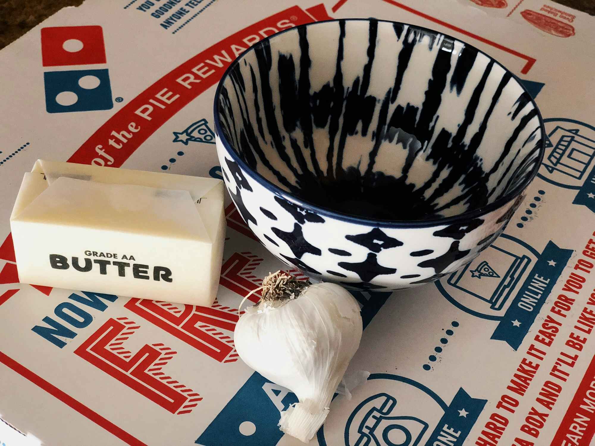 butter a bowl and garlic sitting on top of a pizza box