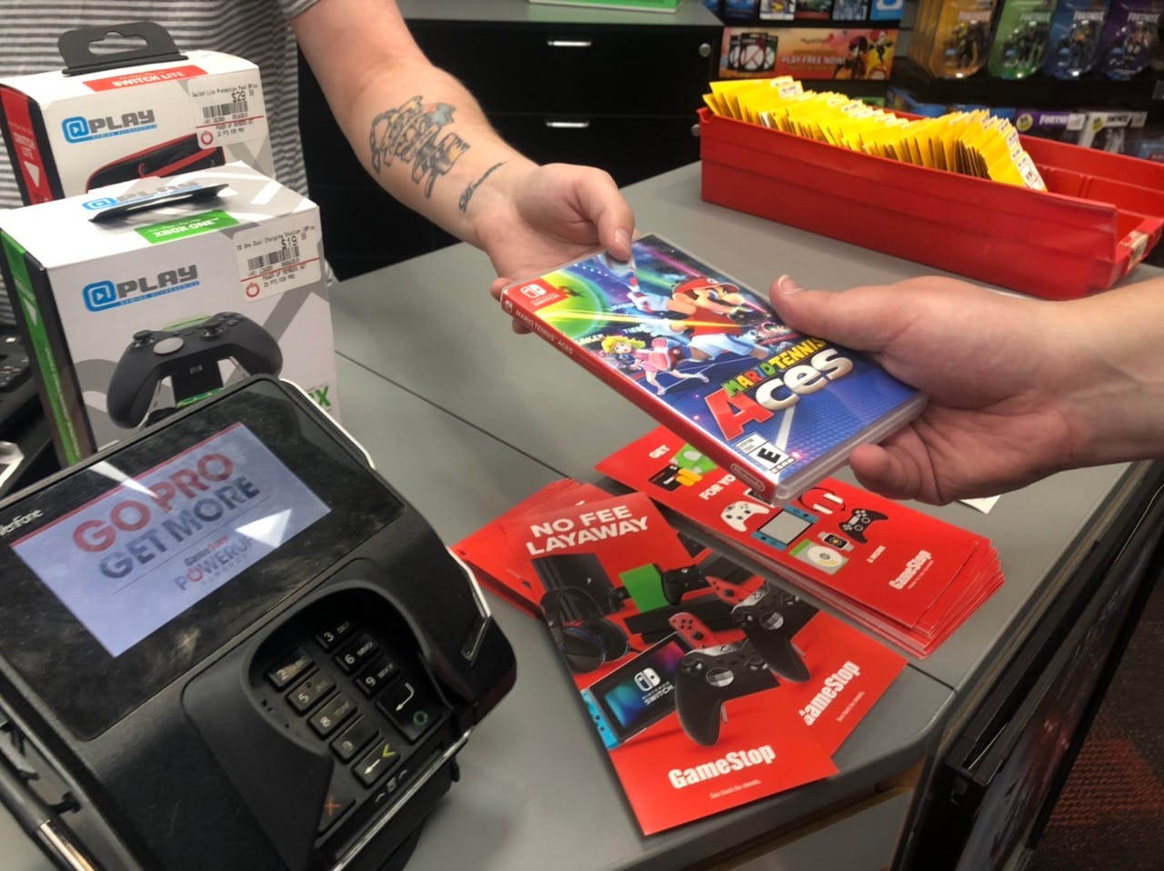 A man hands a video game to another man behind The counter at GameStop.