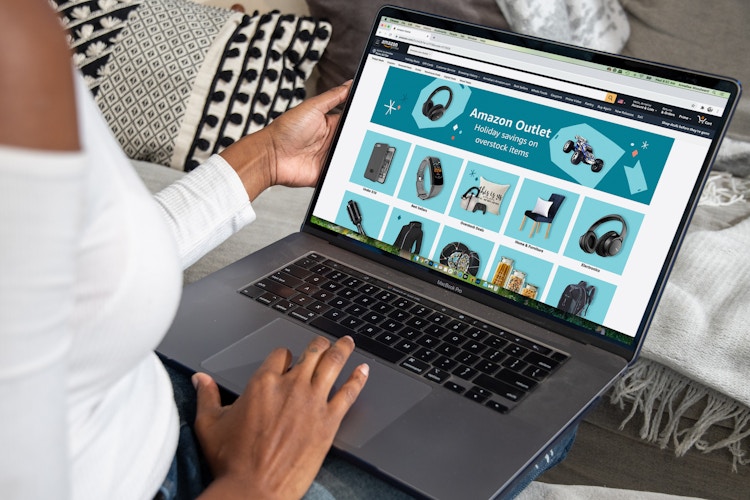 A woman sitting with a laptop on her lap, with Amazon Outlet displayed on the screen.