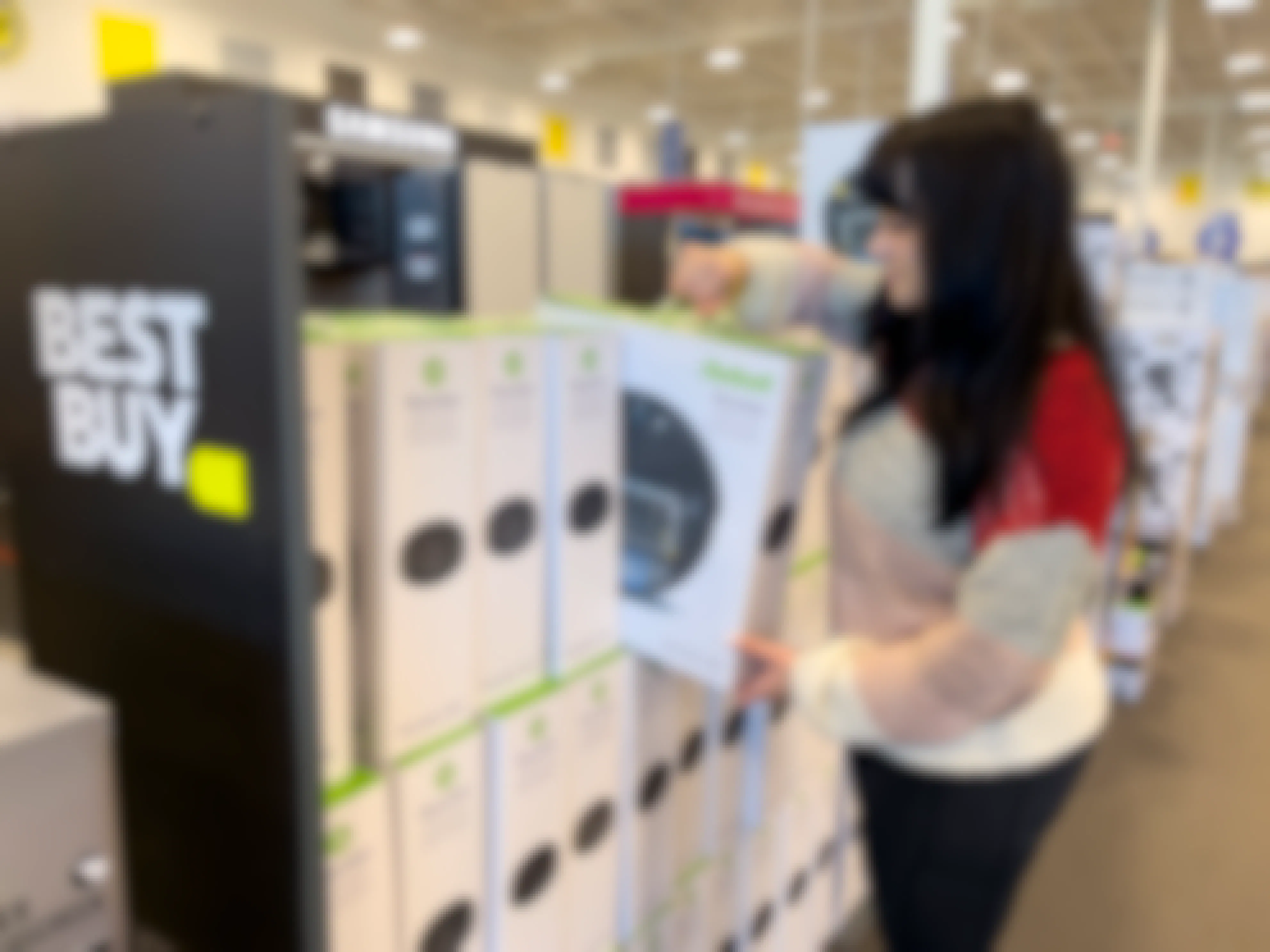 A woman pulling a roomba vacuum from a display at Best Buy.