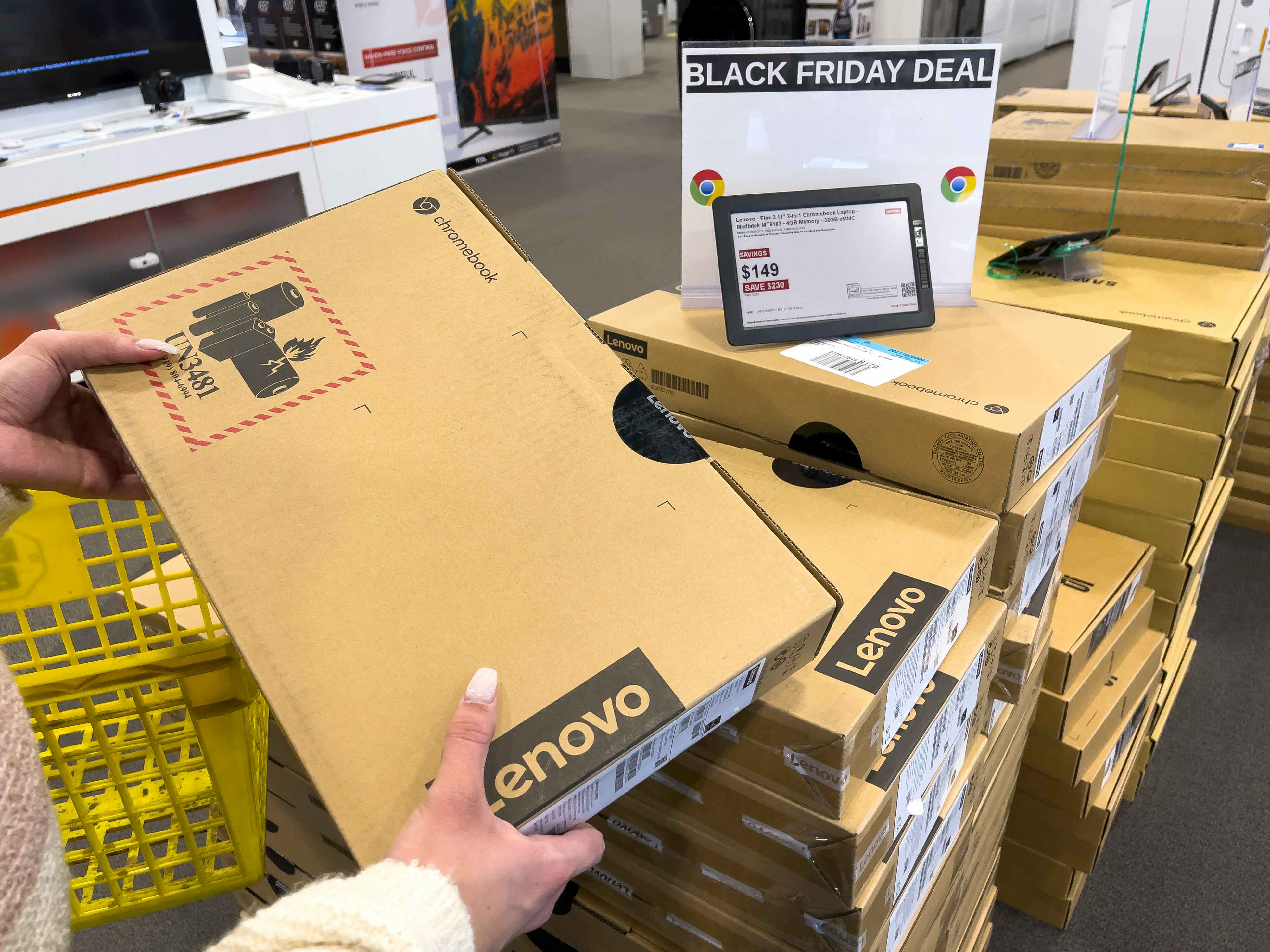 A woman holding a boxed Chromebook computer next to a Black Friday sign at Best Buy.