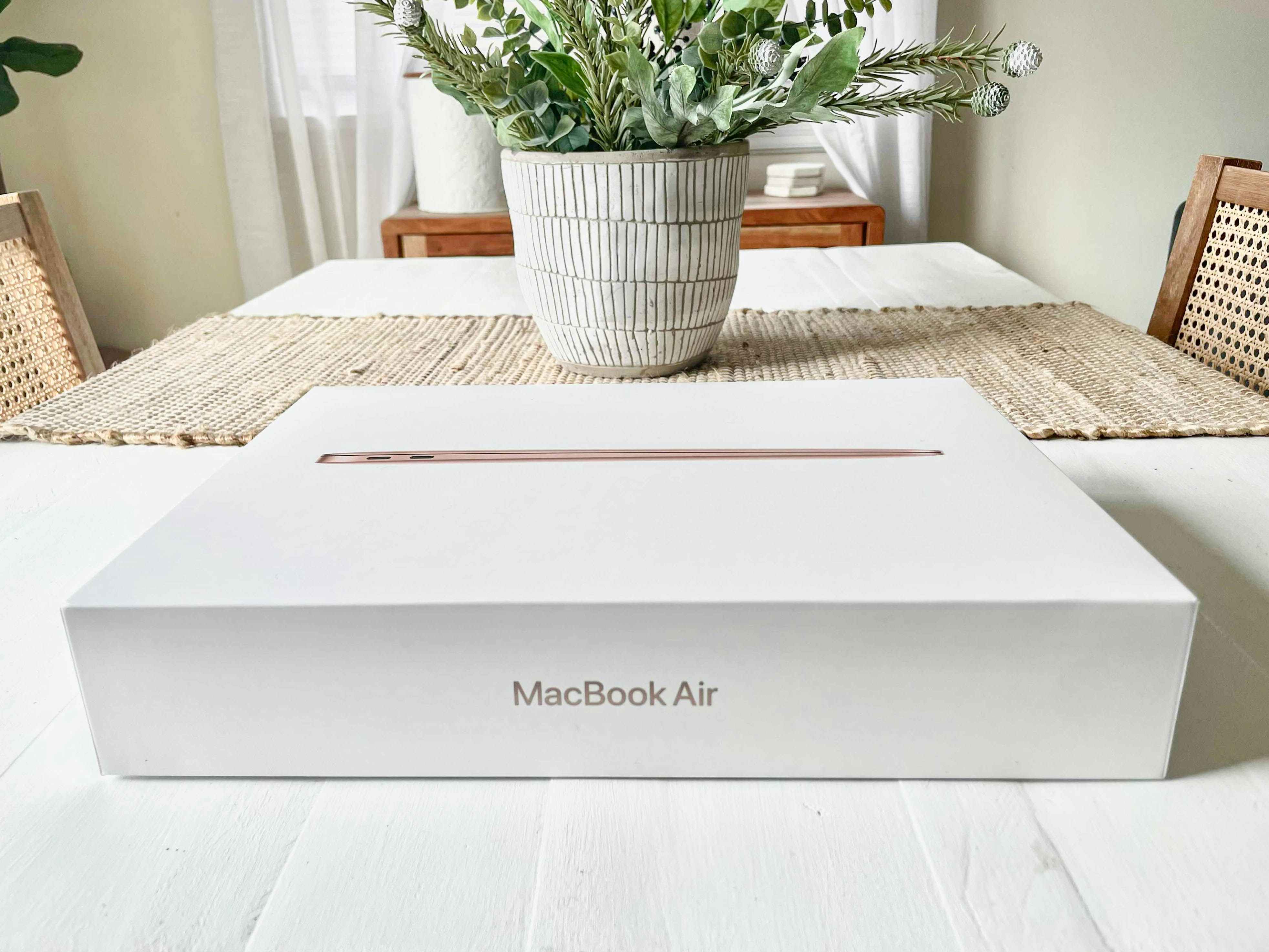 A Macbook box on a table with a plant in the background.