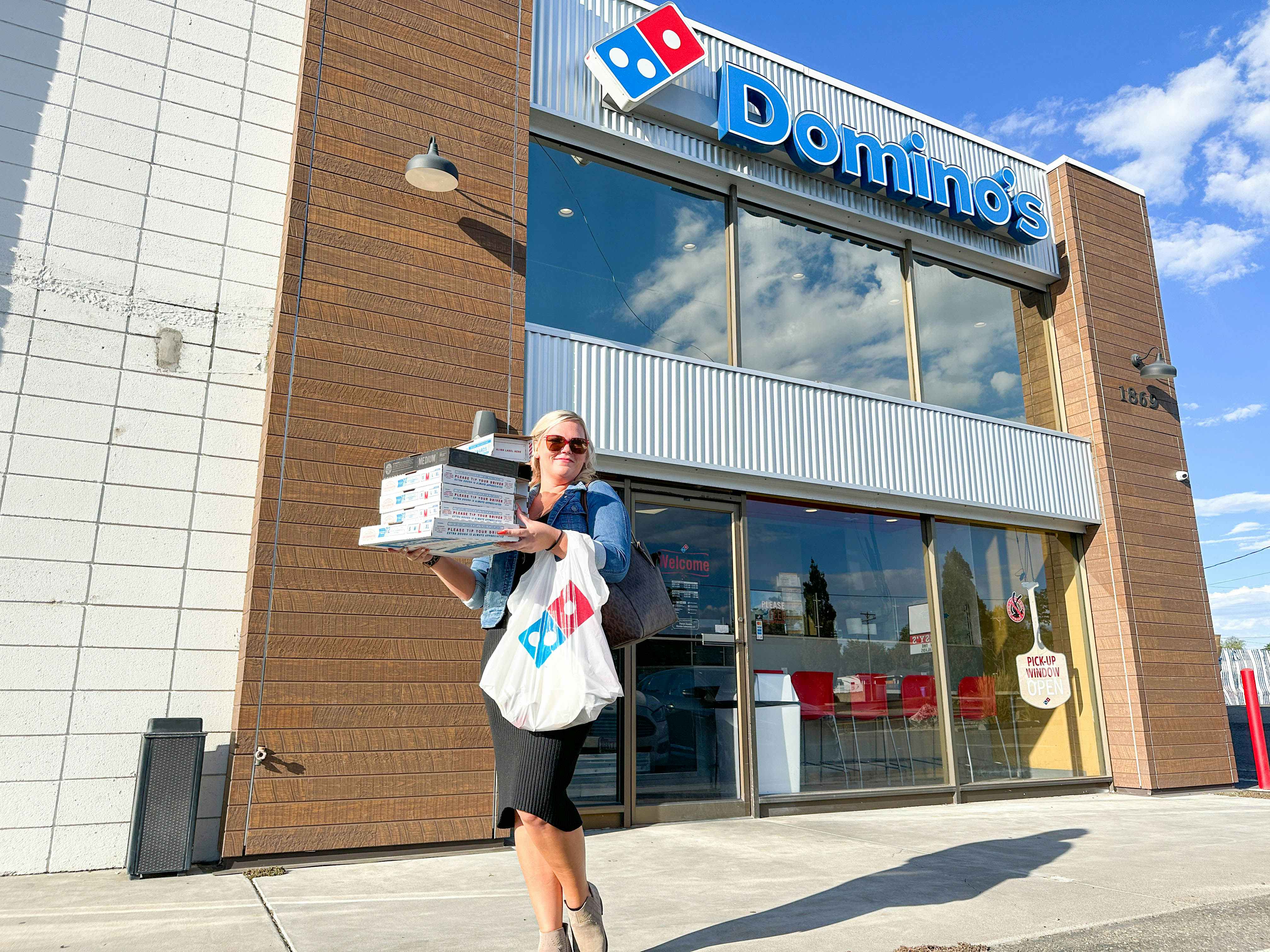 a woman holding a stack of pizza boxes outside dominos