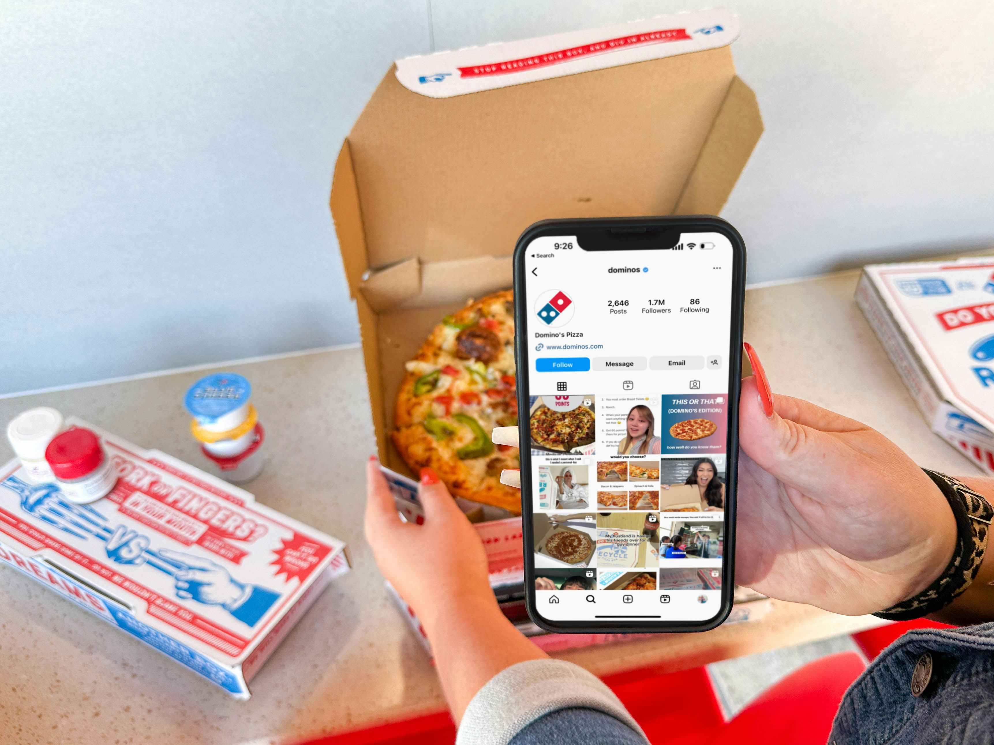 a cellphone with dominos instagram on screen held in front of a pizza 