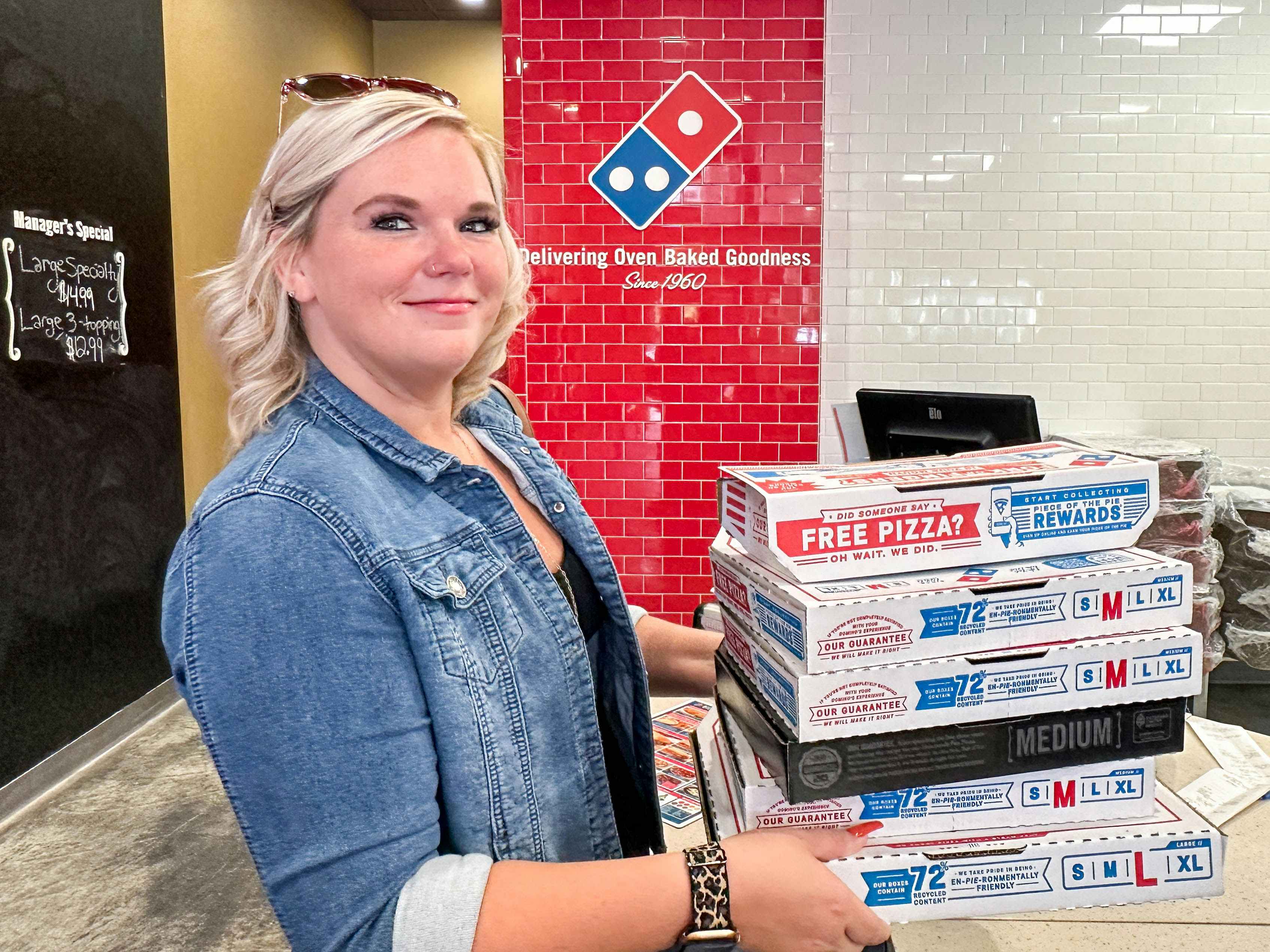 a woman holding a stack of pizza boxes inside dominos