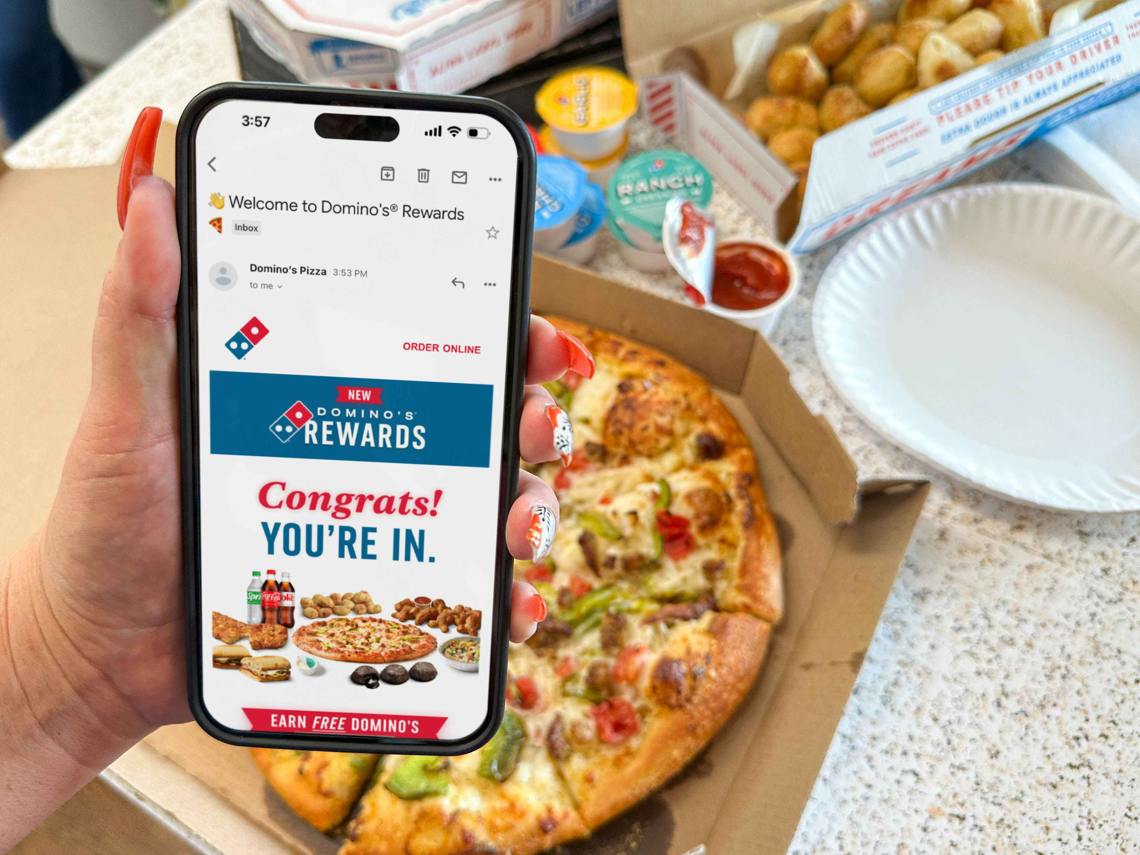 a cellphone being held in front of a pizza with dominos rewards email on screen 