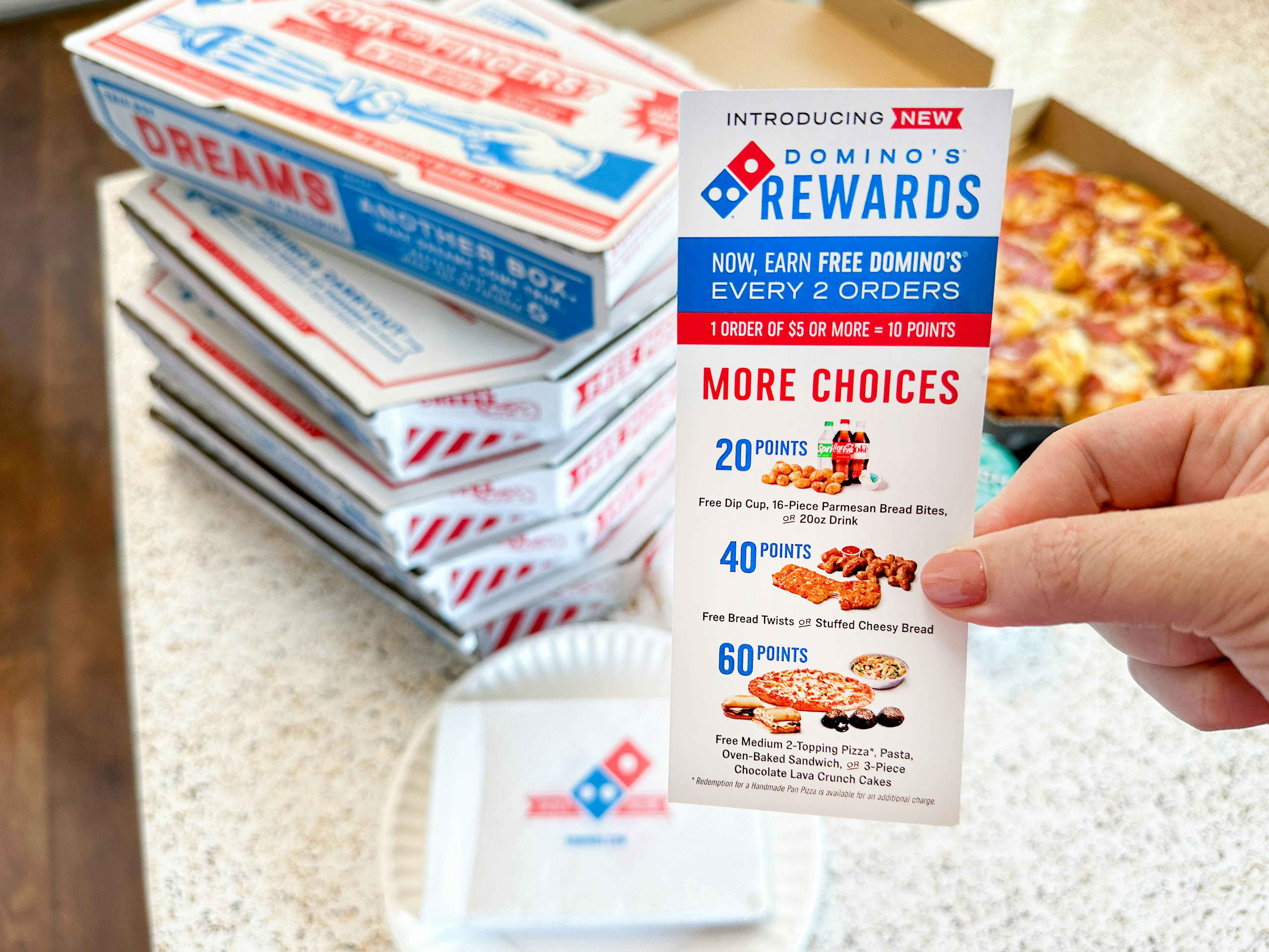 a dominos rewards flyer being held in front of pizza boxes 