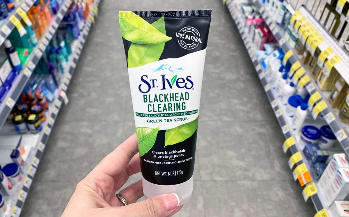 A hand holding St. Ives green tea face scrub in a store aisle