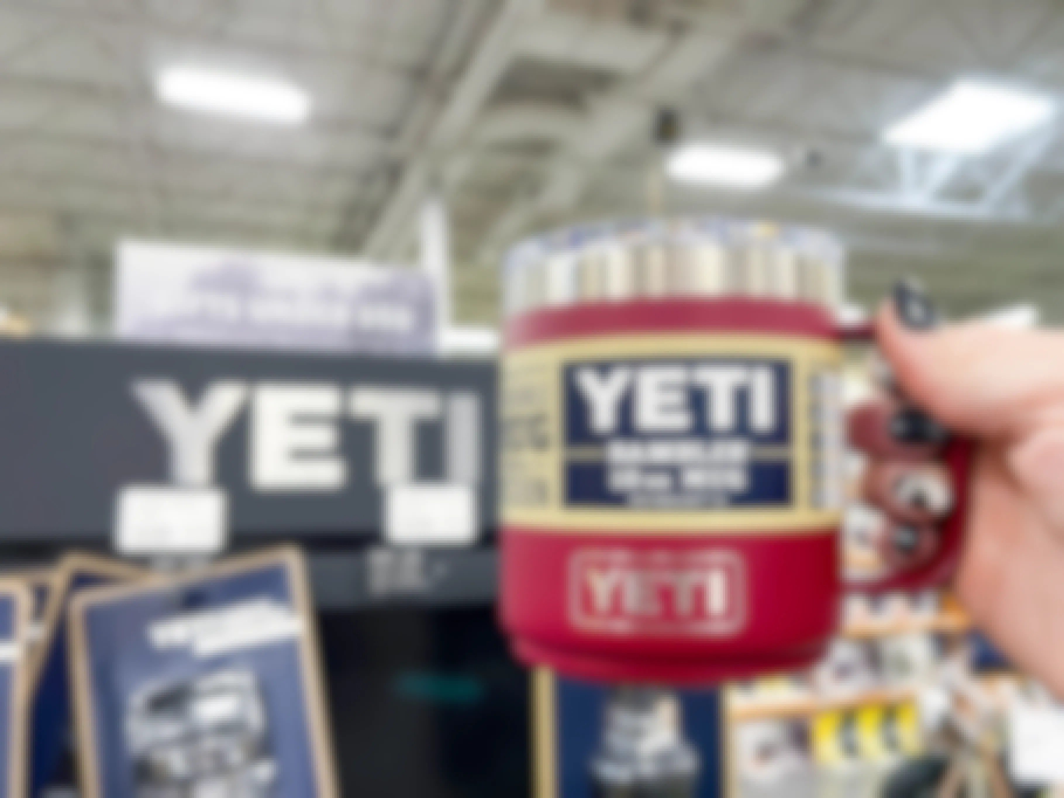 A person's hand holding a Yeti Rambler mug next to a Yeti display inside a store.