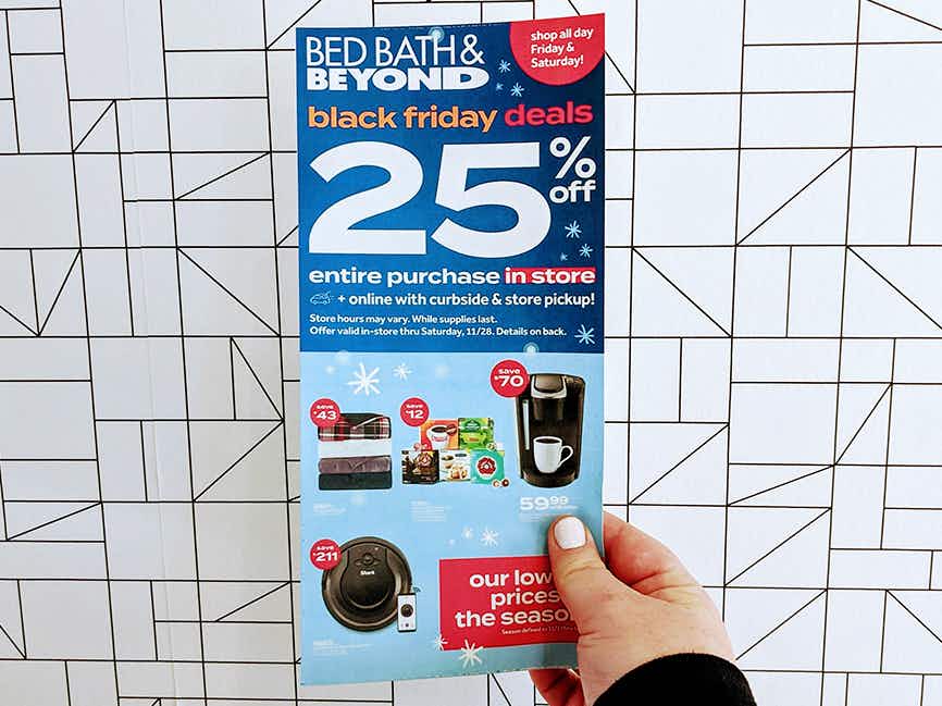 A person holding a Bed Bath and Beyond advertisement in front of a cool wall.