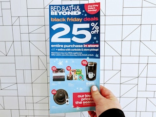 A person holding a Bed Bath and Beyond advertisement in front of a cool wall.