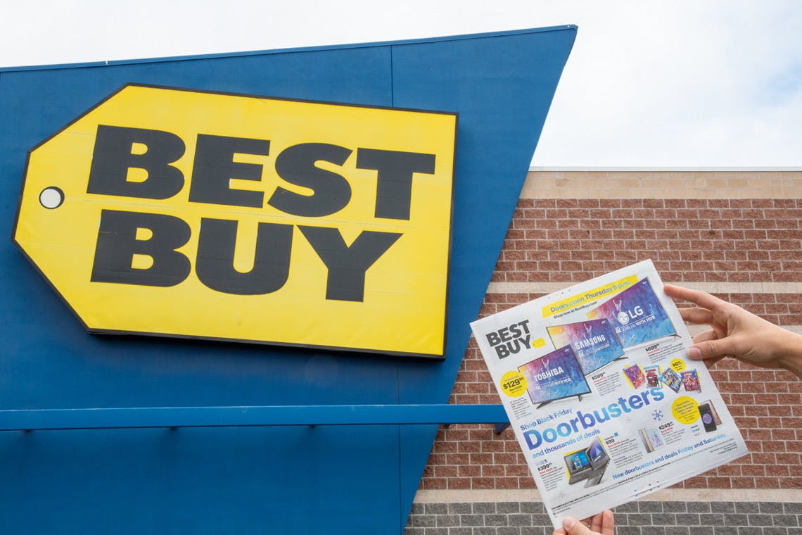 A person holding up a Best Buy Black Friday ad in front of a Best Buy store.