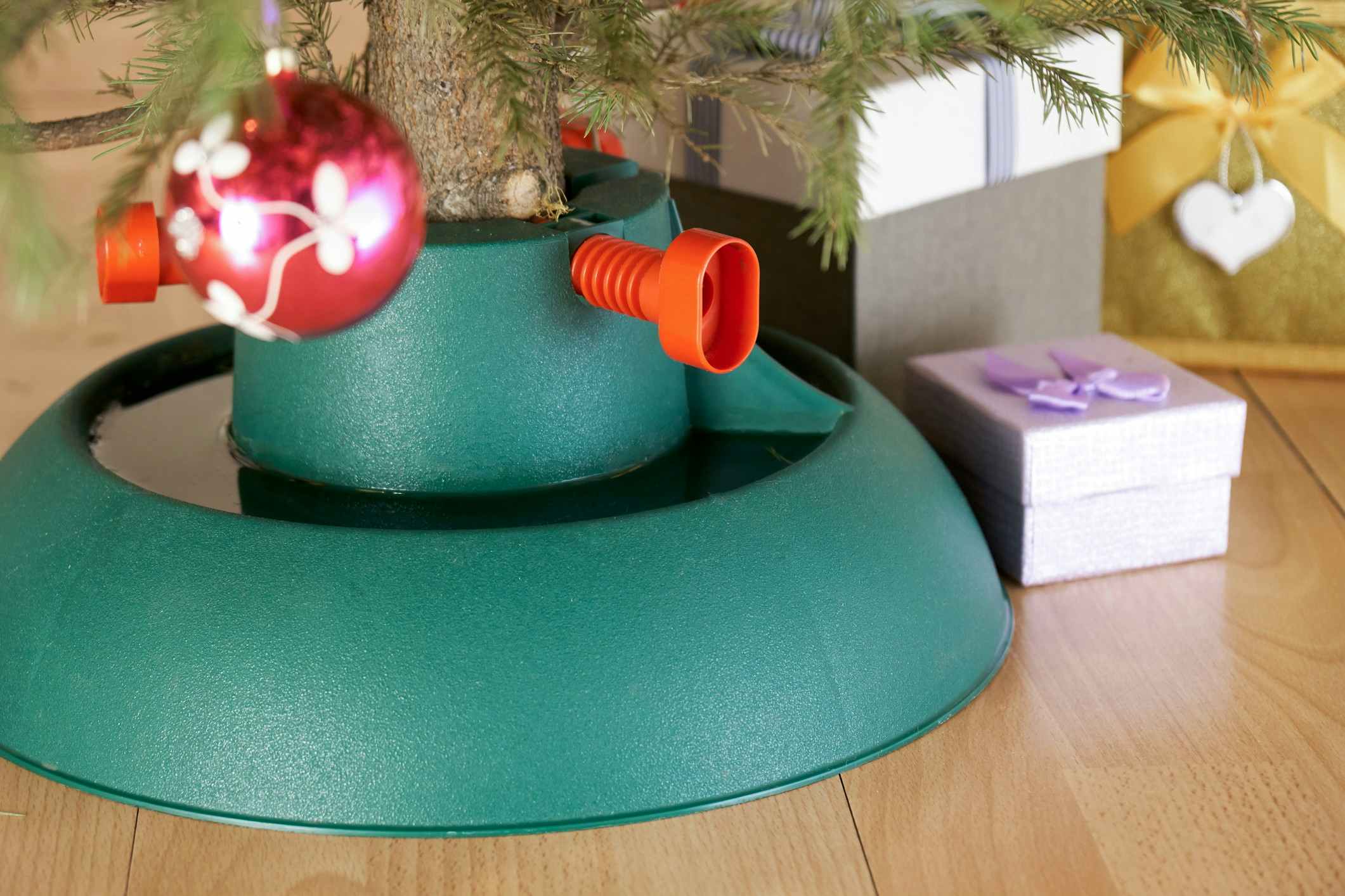 Plastic Christmas tree stand with poured water surrounded by gift boxes stands at home in New Year eve on the floor in city flat