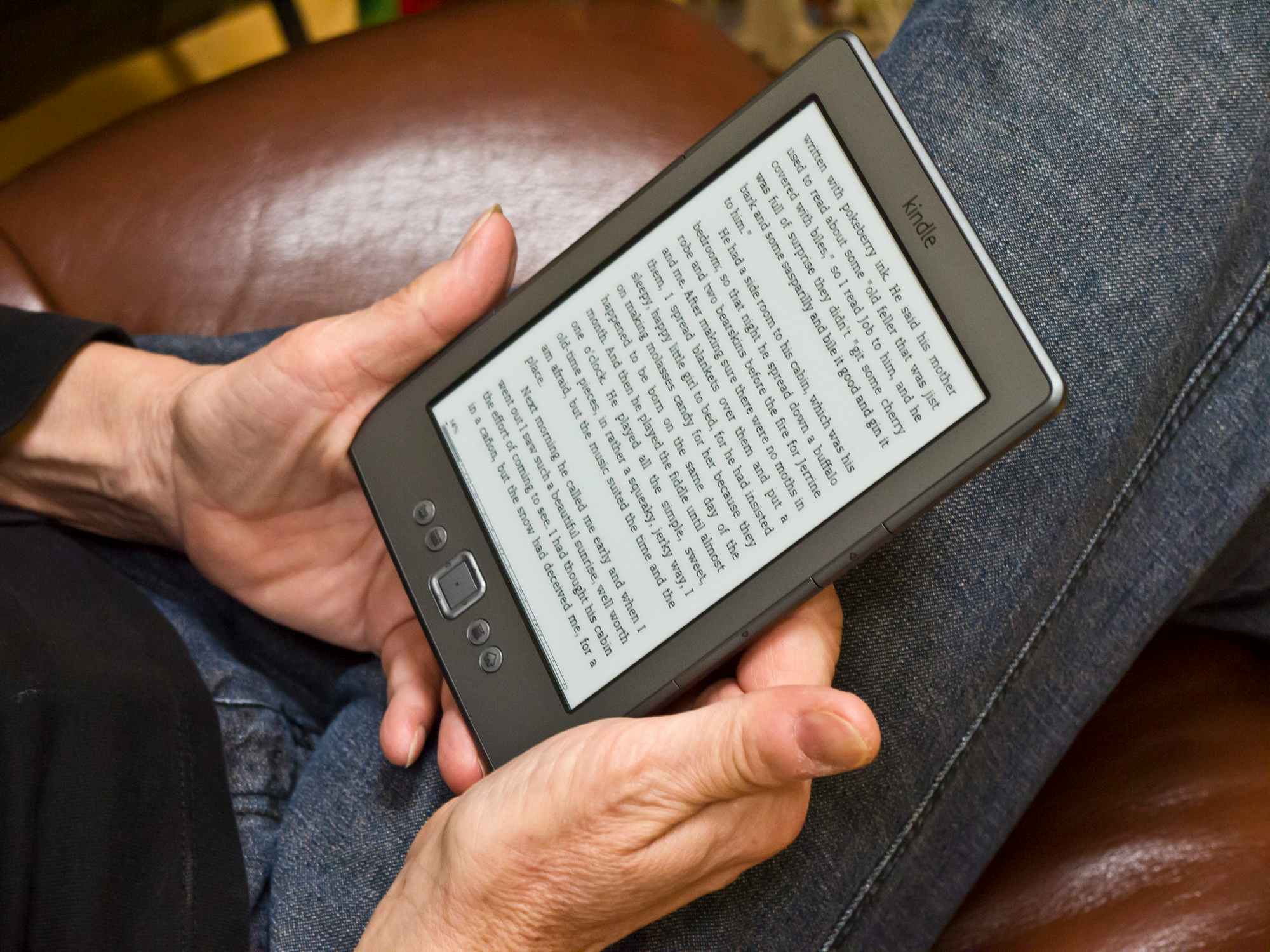 A person sitting on a couch and holding an Amazon Kindle displaying a page of a book.