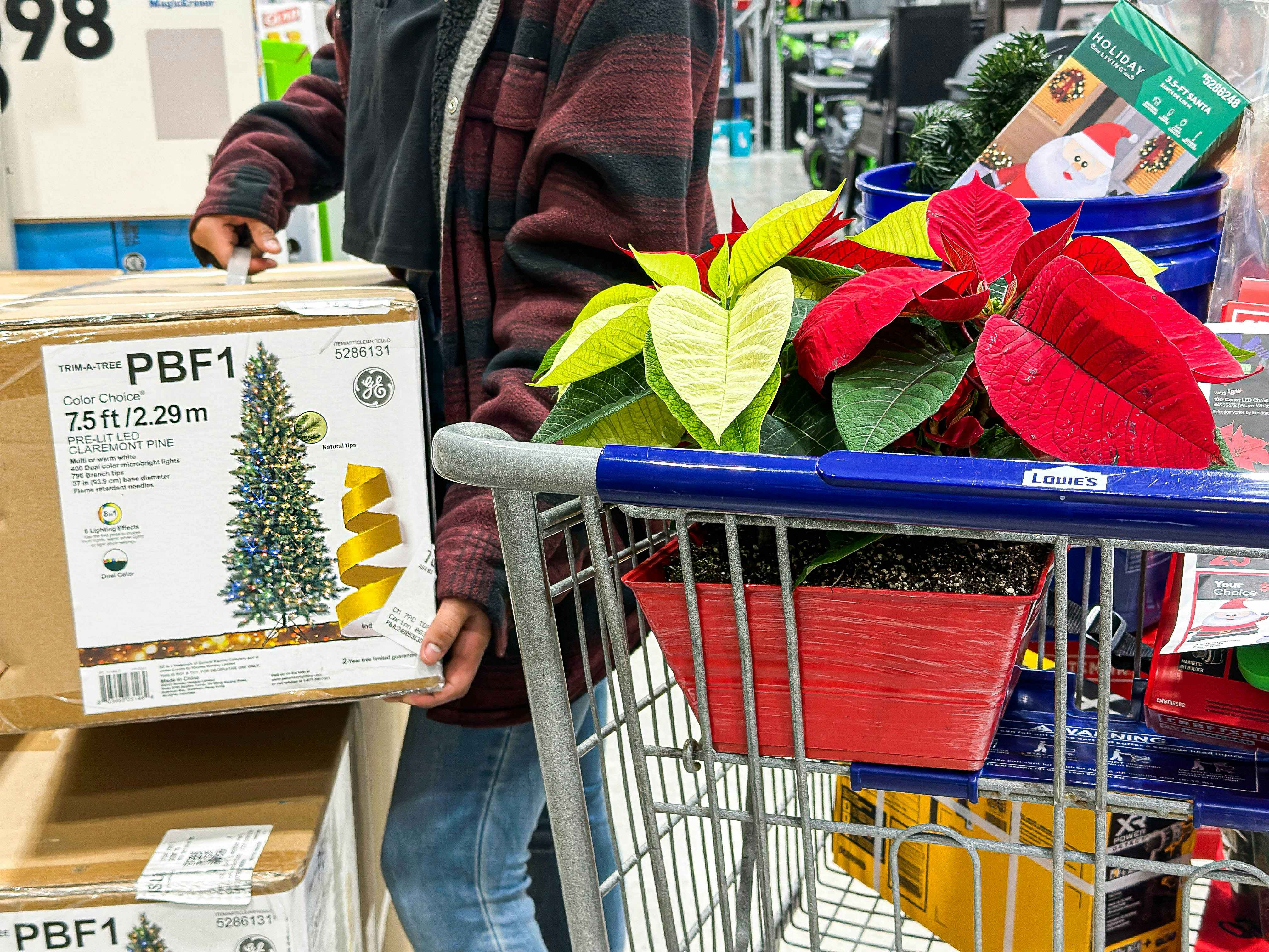 a person lifting a fake christmas tree to place into a lowes cart