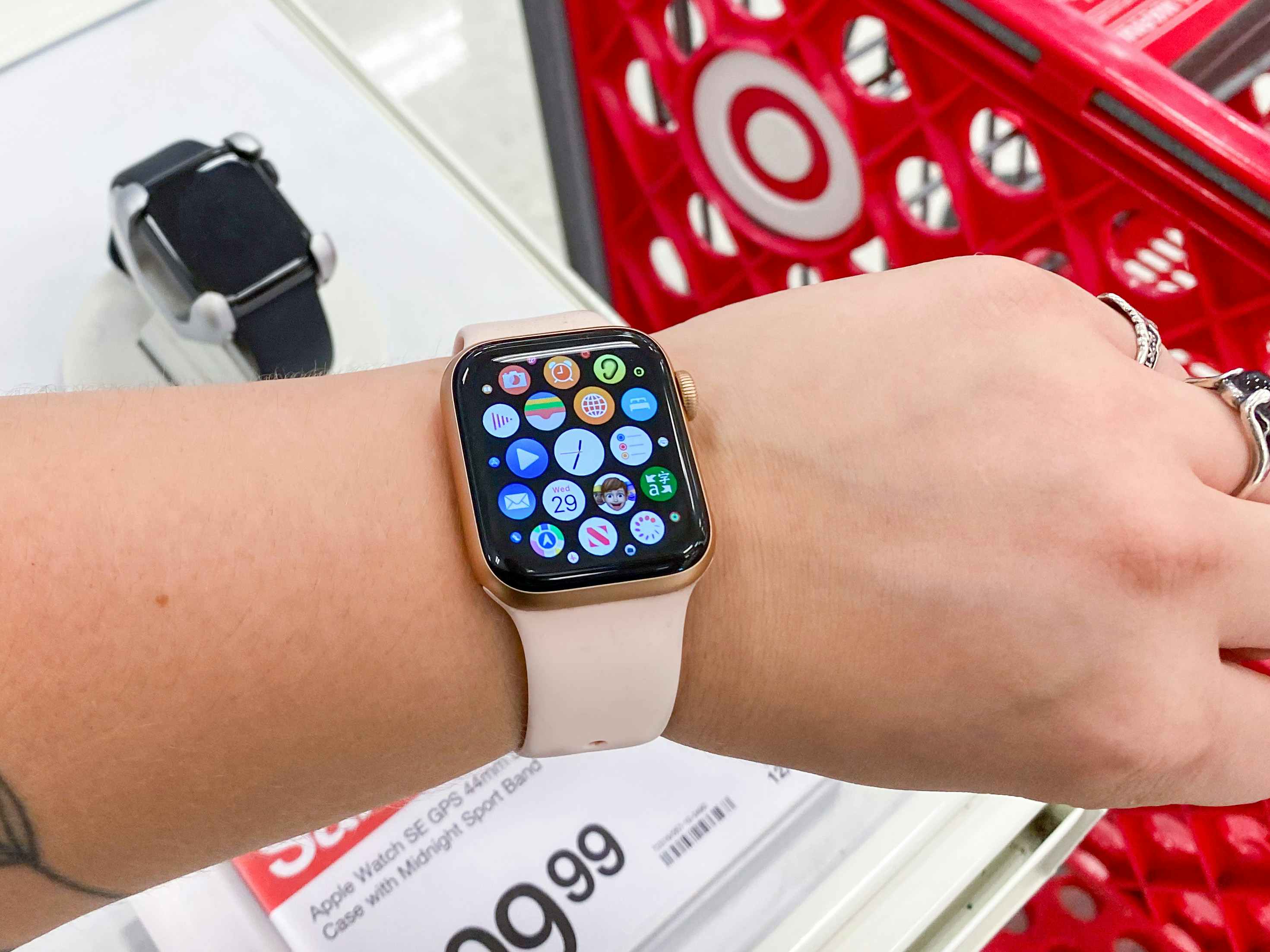 A person holding up their wrist to show their Apple watch in front of the Apple watch display and a Target shopping cart inside Target.