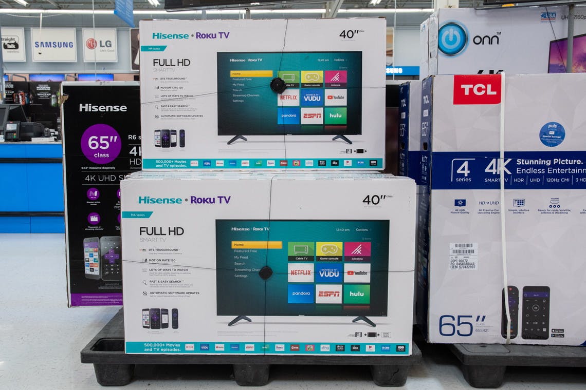 Boxes of HD TVs with Roku TV stacked on a pallet in Walmart's electronics section.