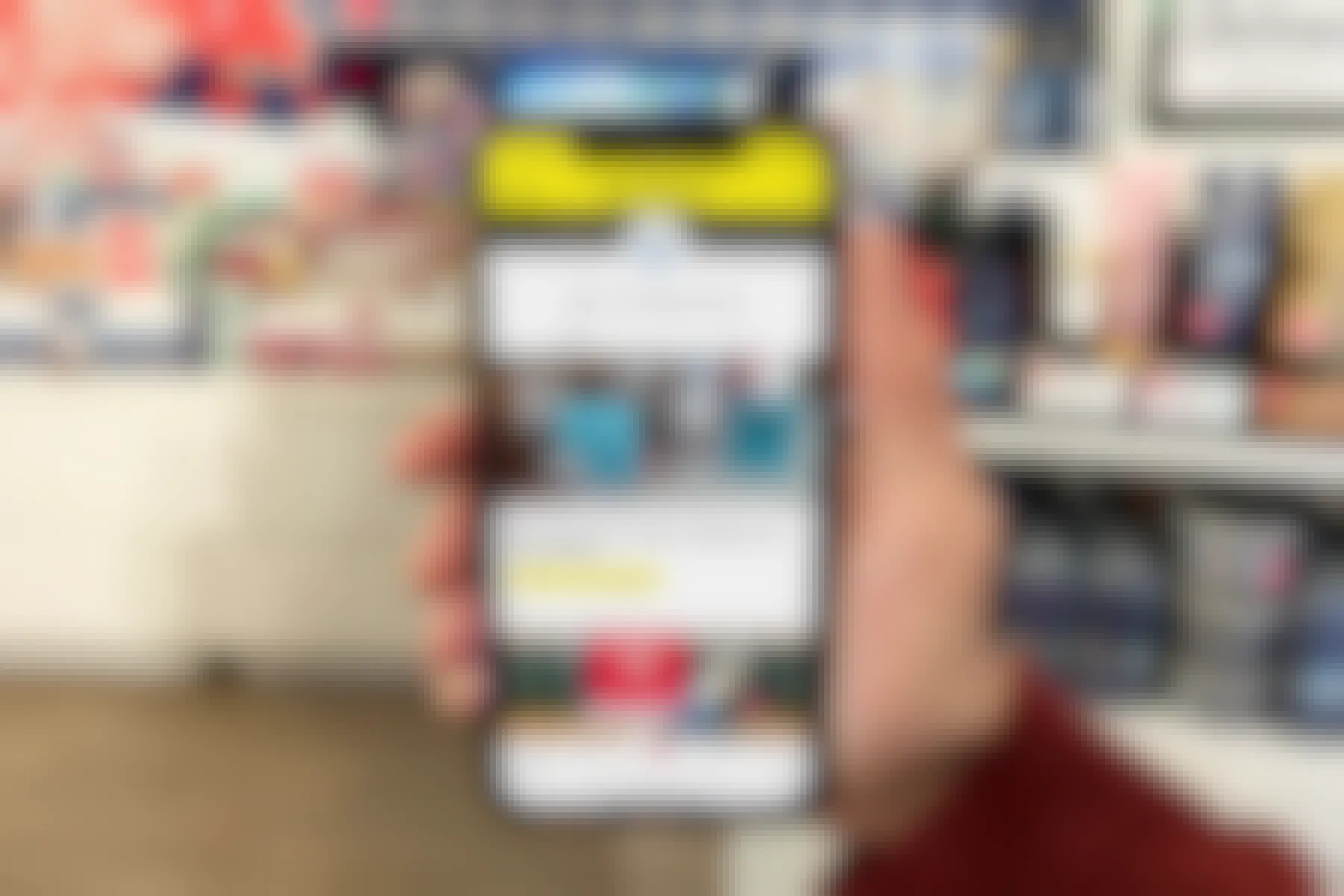 A hand holds a smartphone with the Krazy Coupon Lady app open, showing Bath and Body Works coupons on the screen