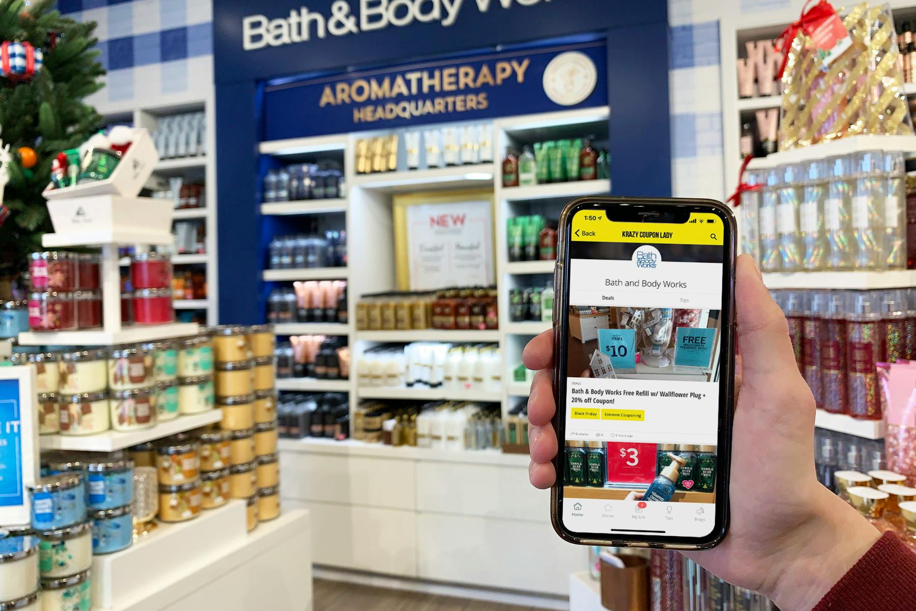 A person's hand holding up a cell phone displaying the KCL app's Bath & Body Works page inside a Bath & Body Works store.