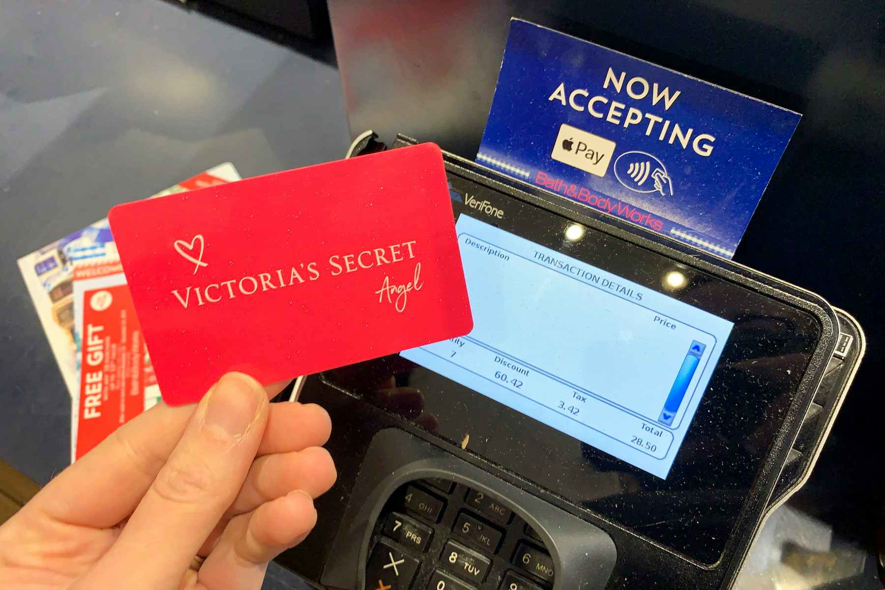 A person's hand holding their Victoria's Secret Angel Card above the point-of-sale machine at Bath & Body Works.