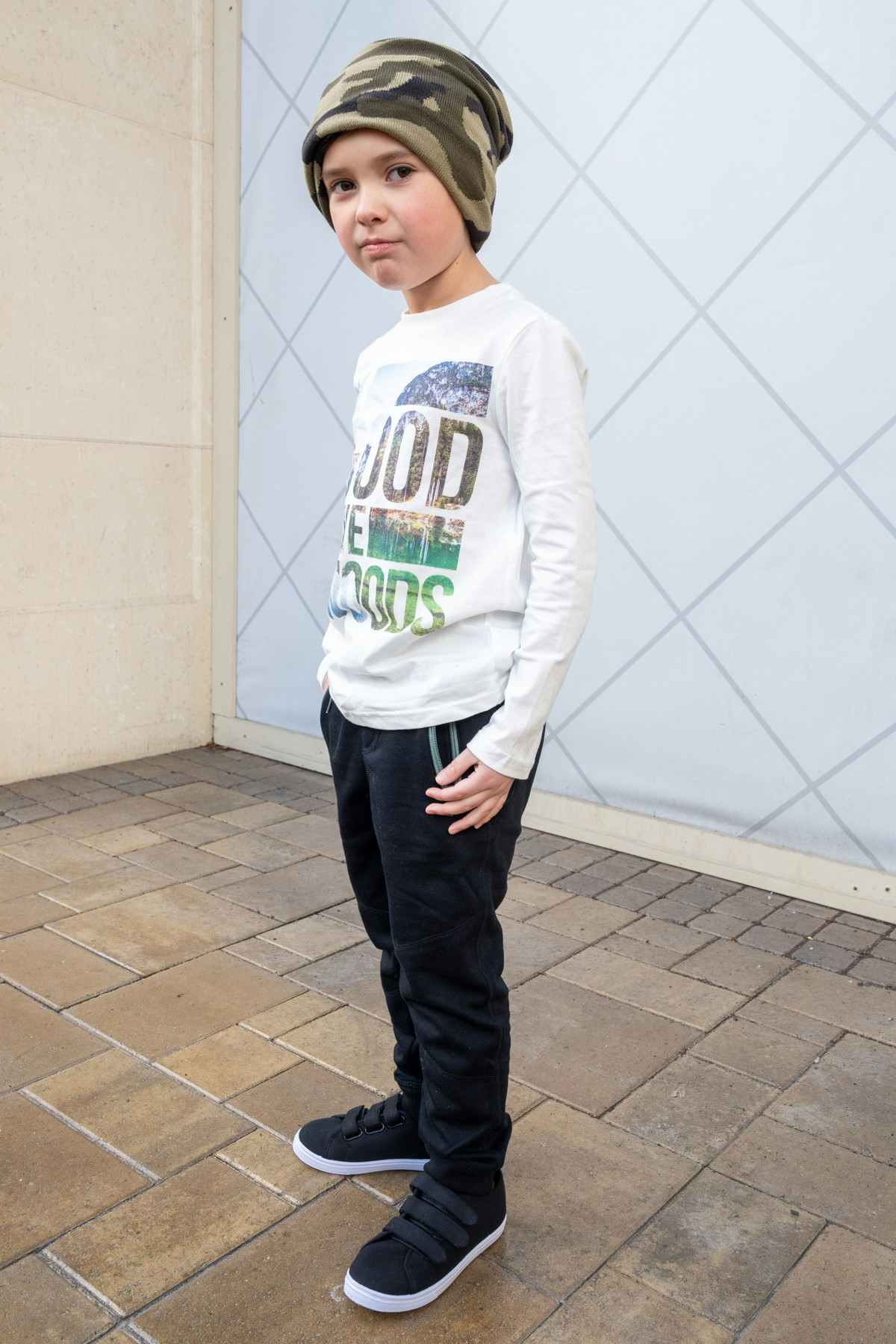 Boy wearing FabKids Wild Woods Outfit white long sleeve t-shirt, black kids joggers and camo beanie