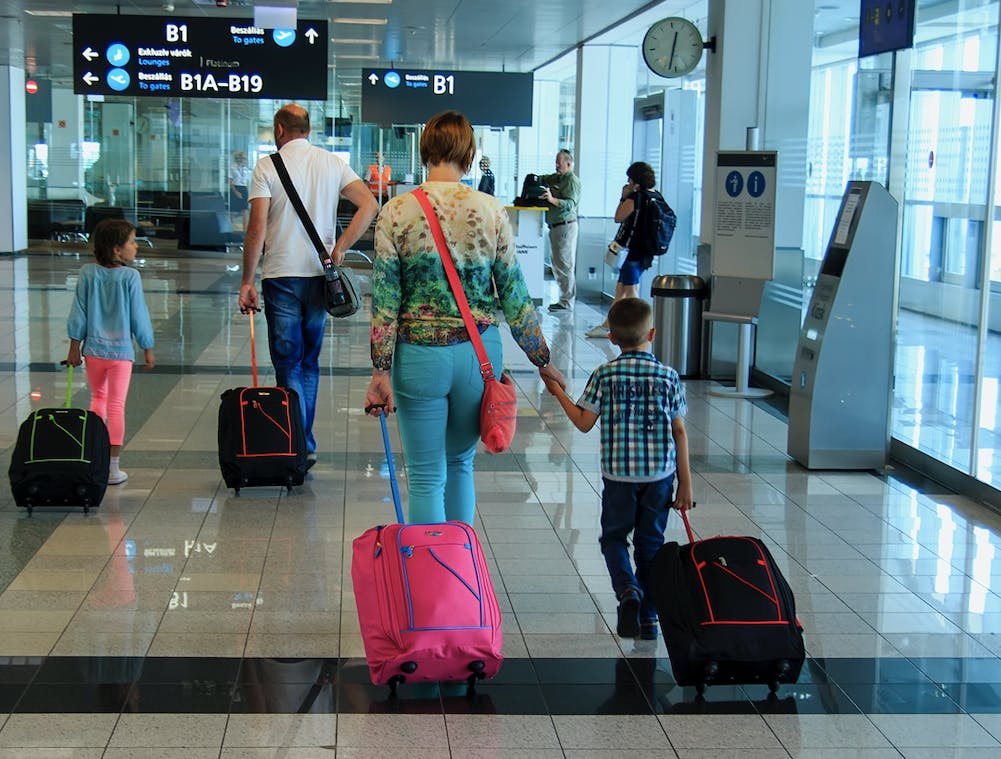A woman and child walk through an airport with rolling suitcases