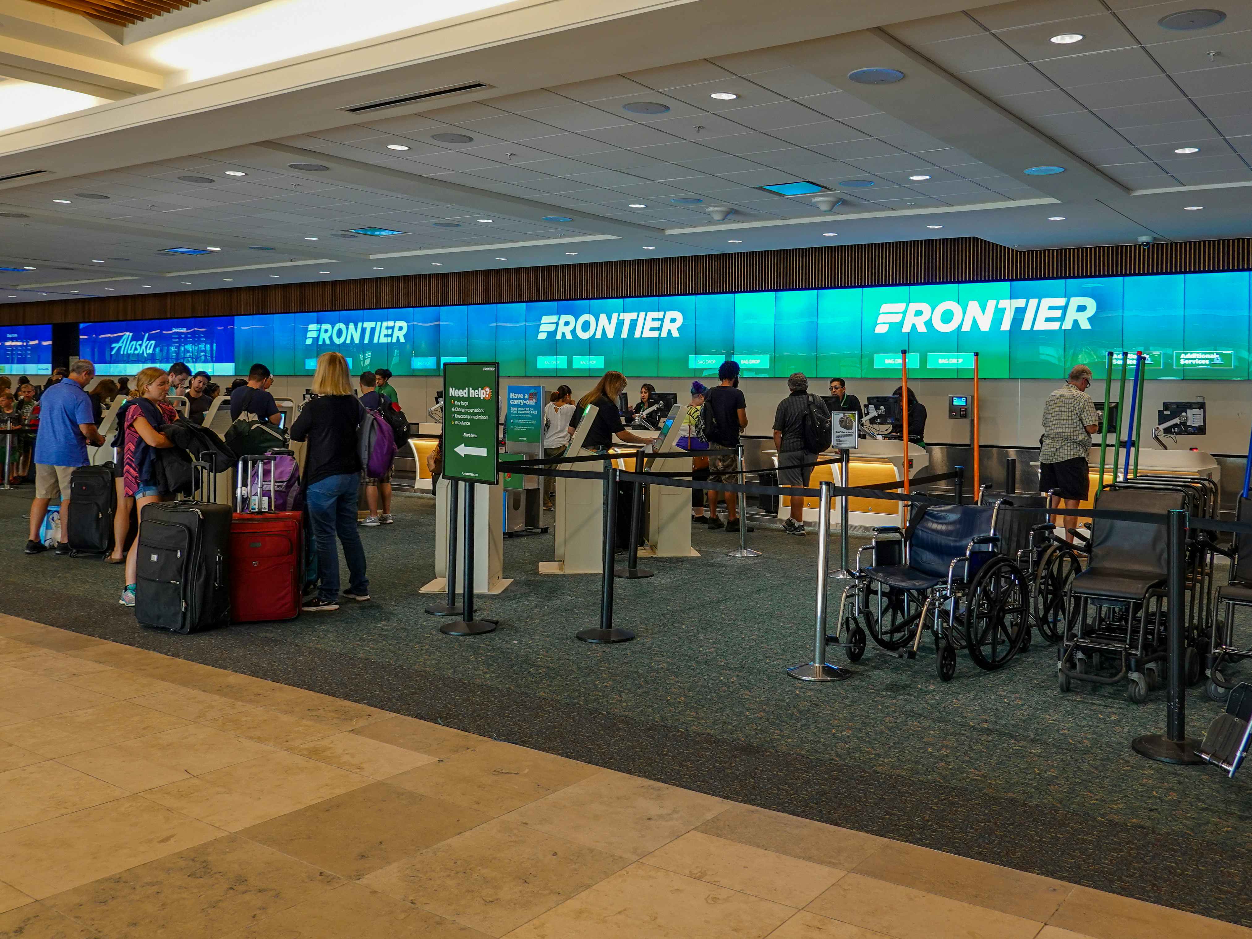 People standing near the check-in desks for Frontier in the airport.