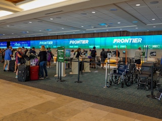 People standing near the check-in desks for Frontier in the airport.