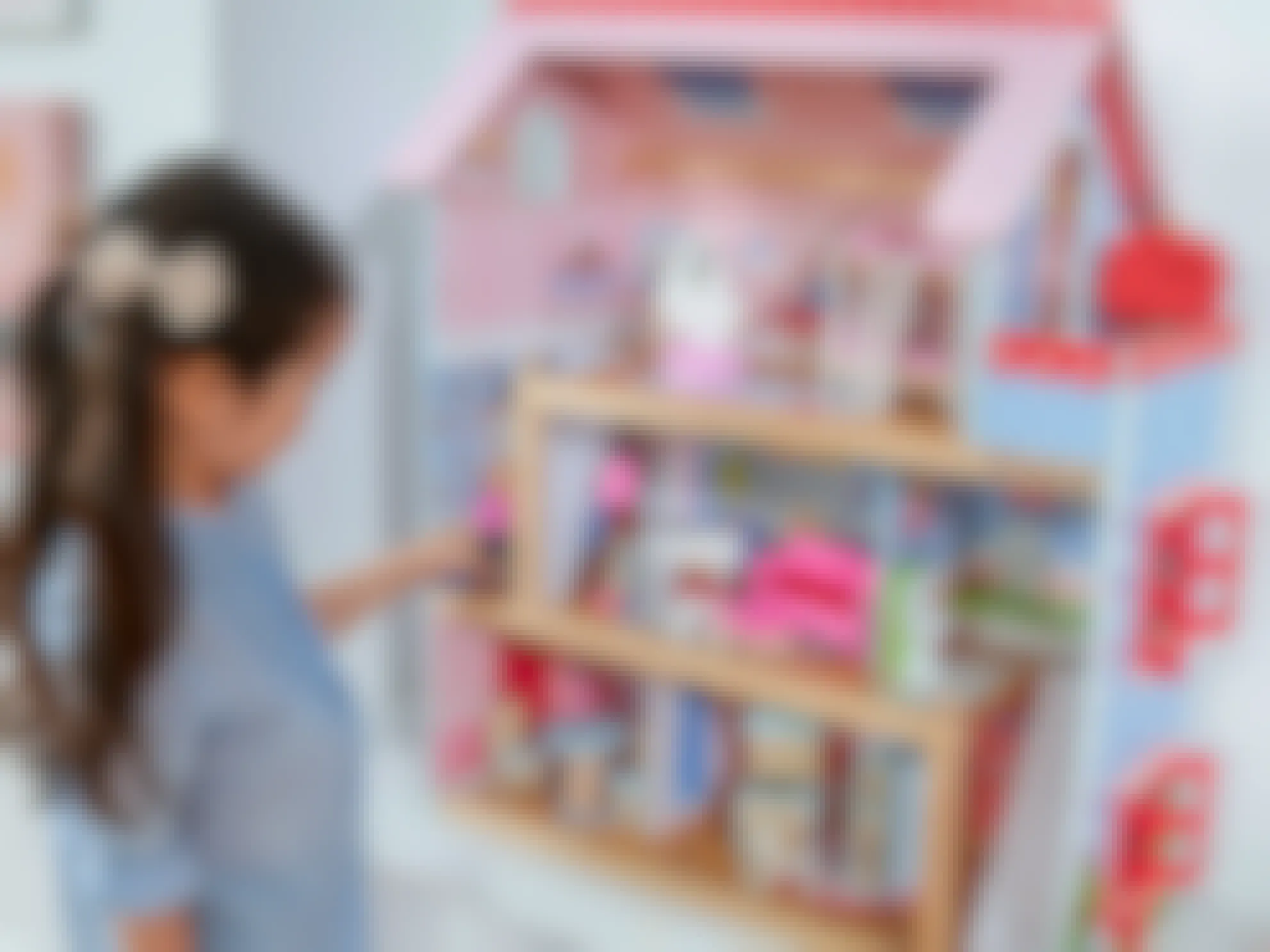A little girl playing with a KidKraft Wooden Dollhouse in a bedroom.
