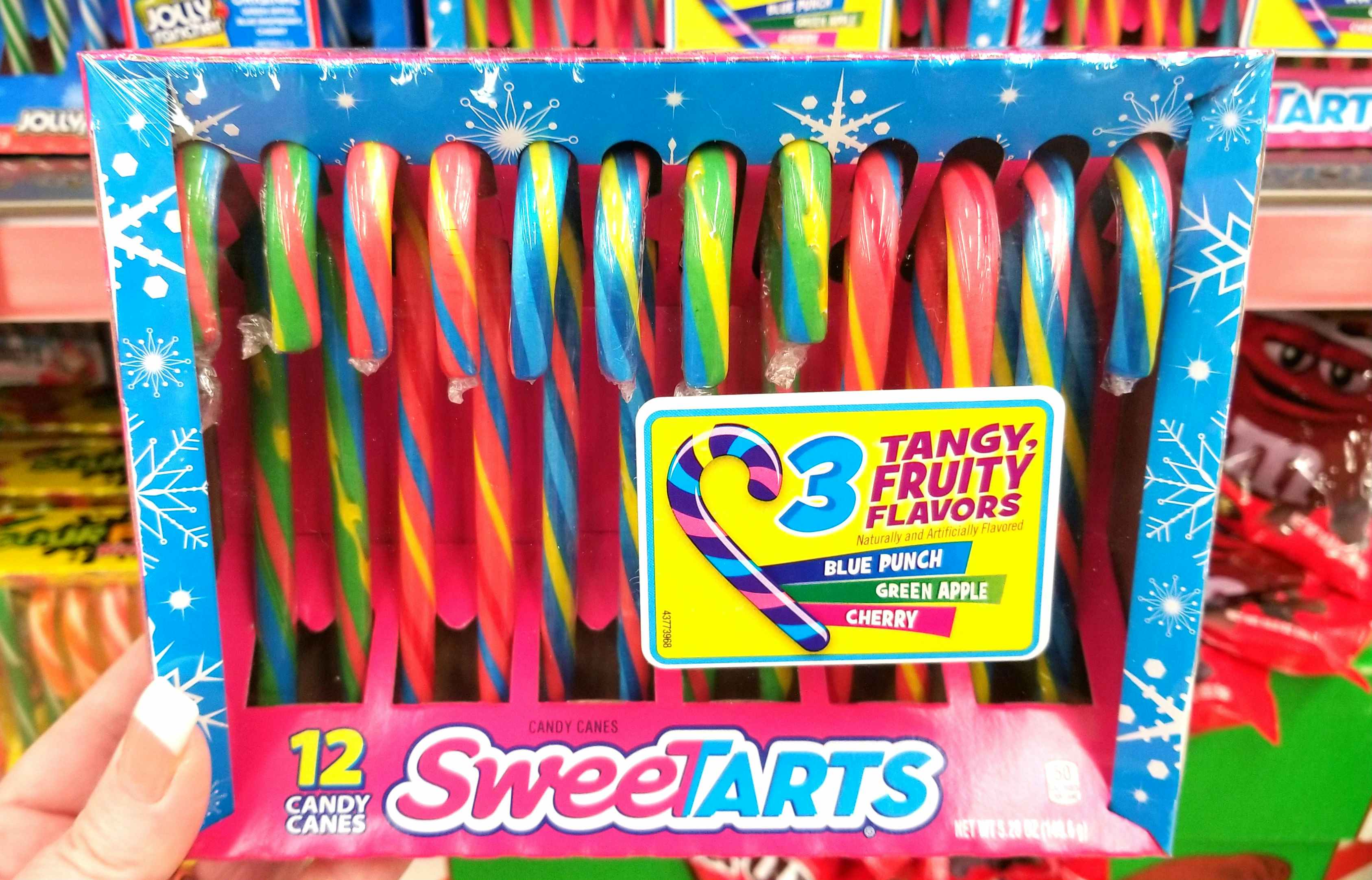 A person holding a packages of Sweetart candy canes.